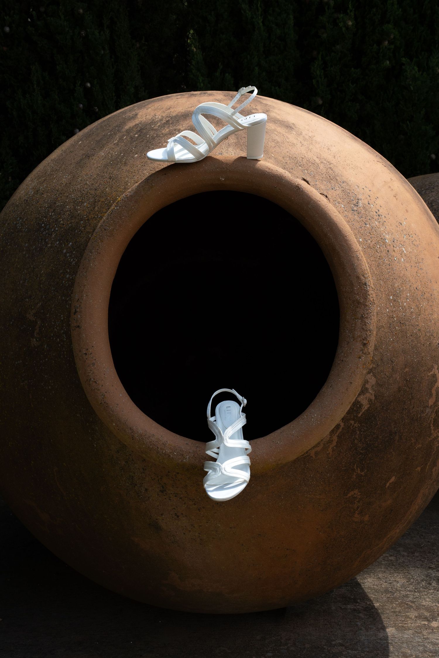 White bridal strappy heeled sandals displayed on a large rustic terracotta clay pot outdoors. Mallorca wedding photographer.