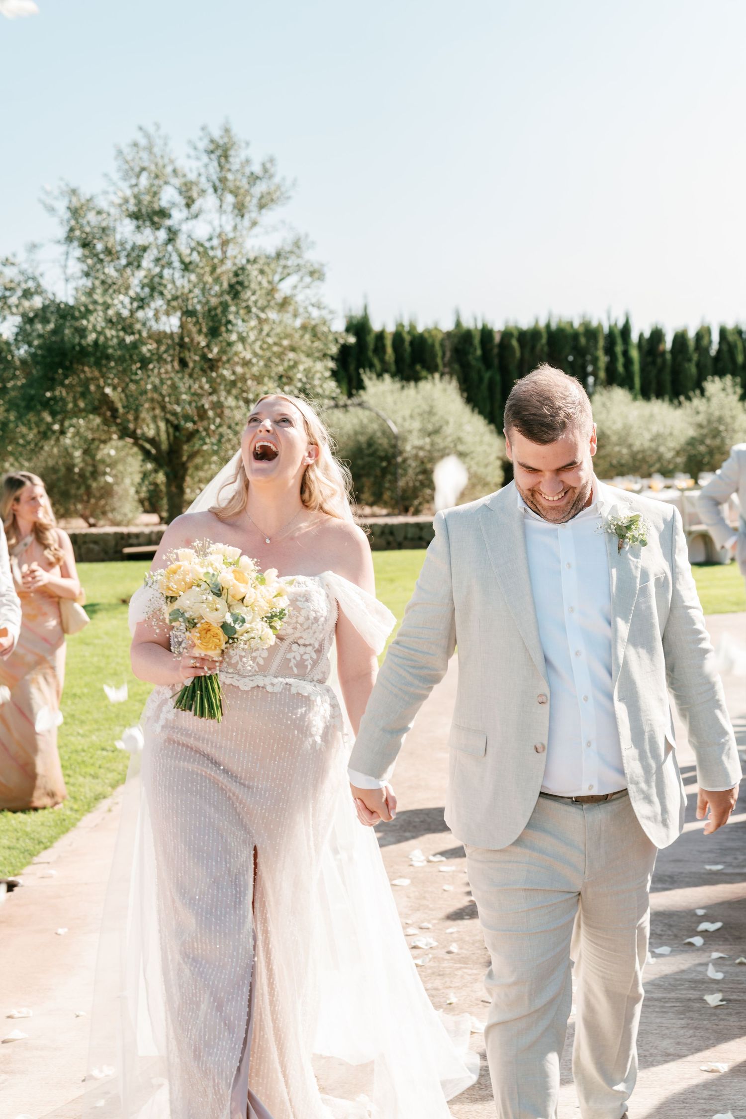 Joyful bride and groom walk hand-in-hand after outdoor wedding ceremony, bride holding yellow bouquet. Mallorca wedding photographer