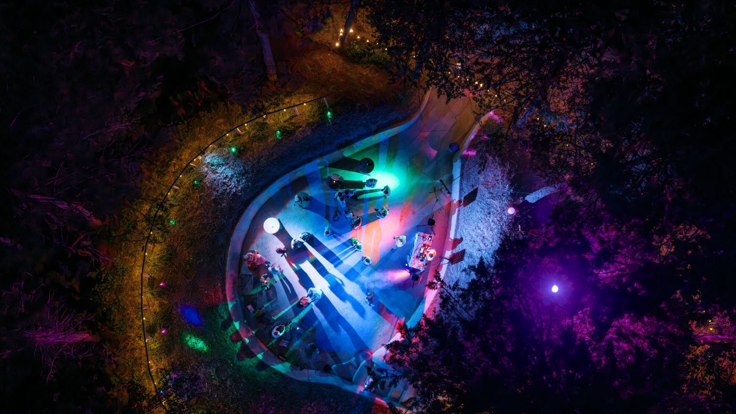Aerial view of colorful illuminated outdoor amphitheater surrounded by trees at night.