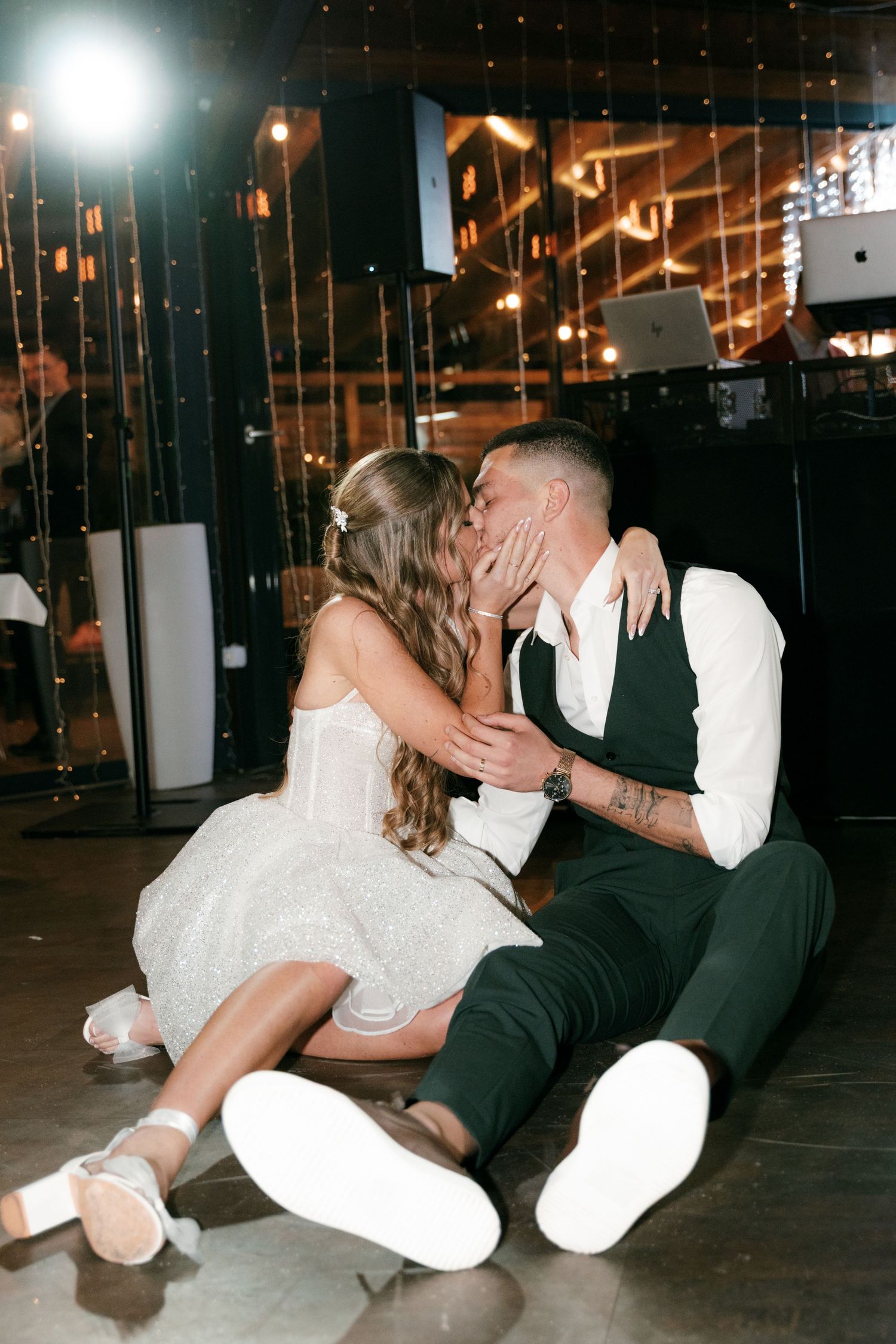 Bride and groom share a playful kiss while sitting on the dance floor surrounded by glittering lights. Mallorca wedding photographer