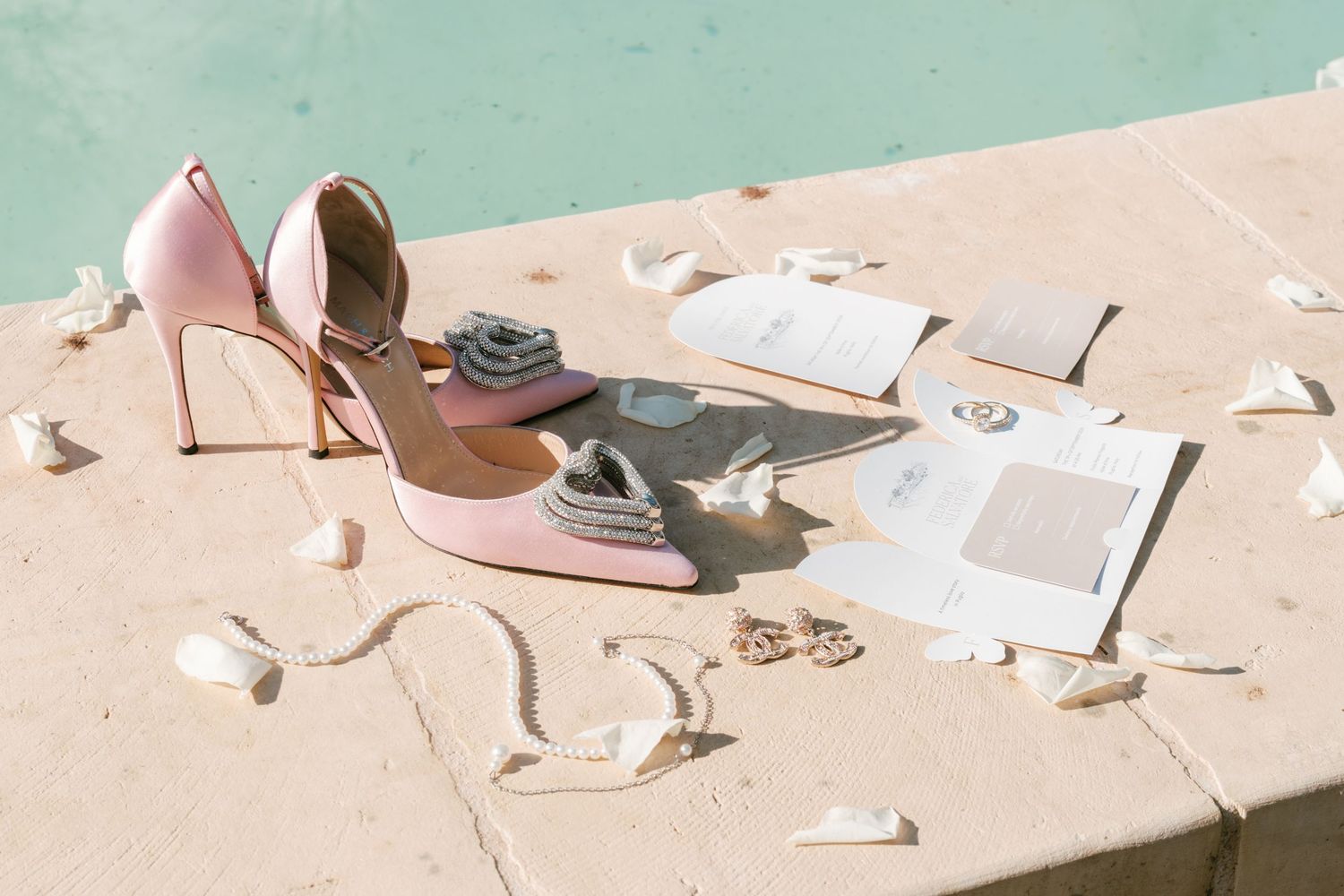 Pink bridal heels styled with wedding stationery and flower petals on a stone surface. Puglia wedding photographer, film
