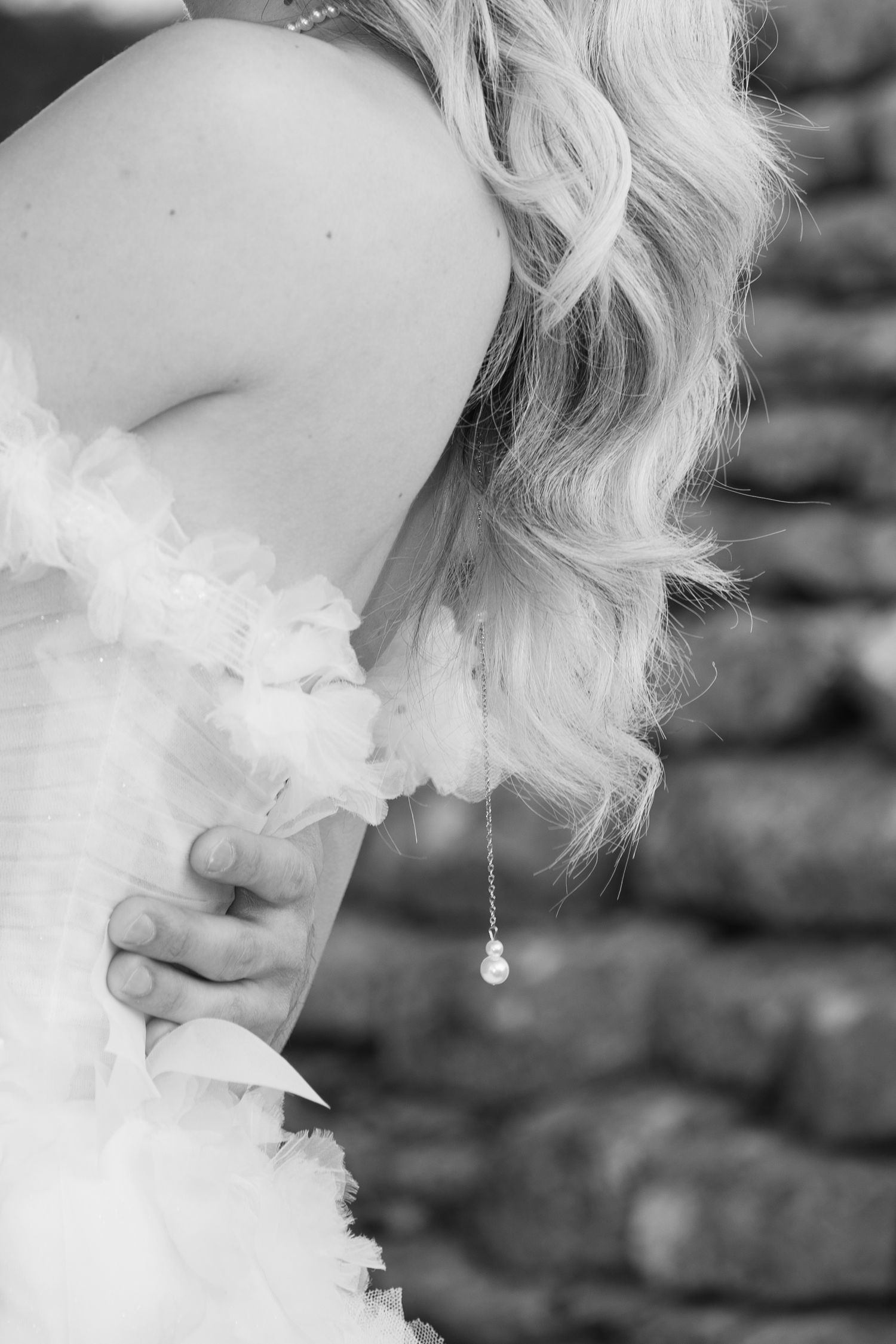 Black and white close-up of bride in ruffled wedding gown with pearl drop necklace detail. Puglia wedding photographer, film
