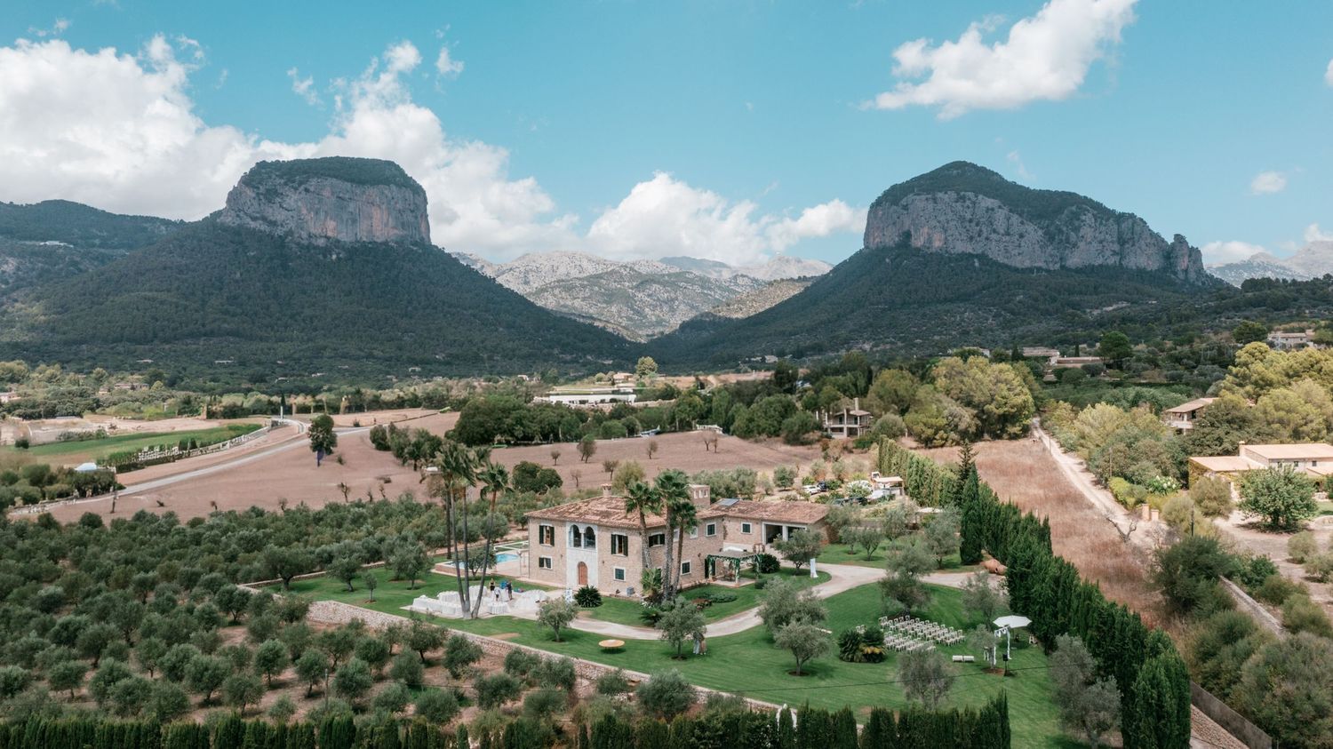 Aerial view of a luxury Mediterranean villa on Mallorca surrounded by olive trees with dramatic rocky mountains in the background. Mallorca