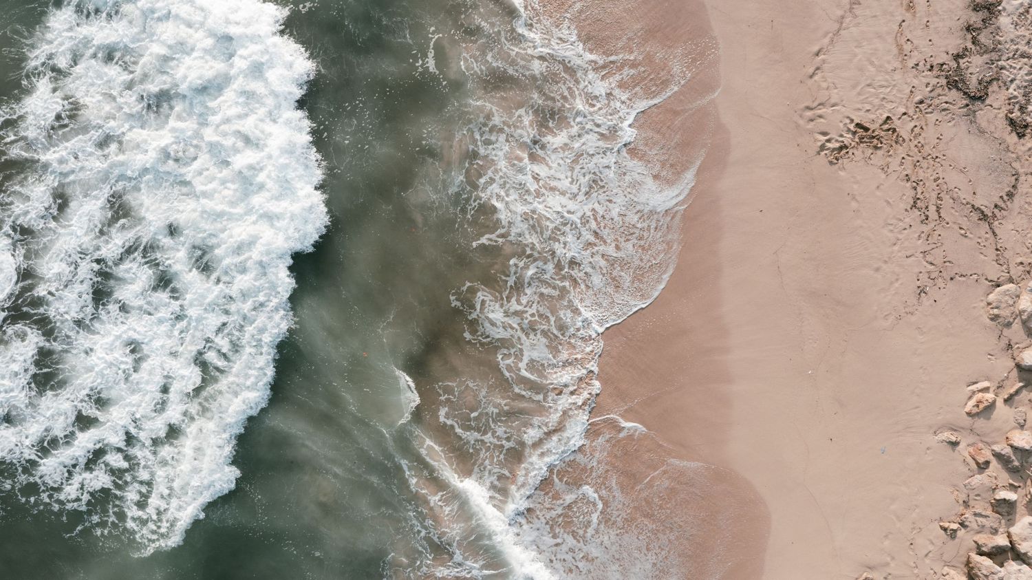 Aerial drone view of ocean waves washing onto a sandy beach shoreline. Mallorca wedding photographer, filmmaker