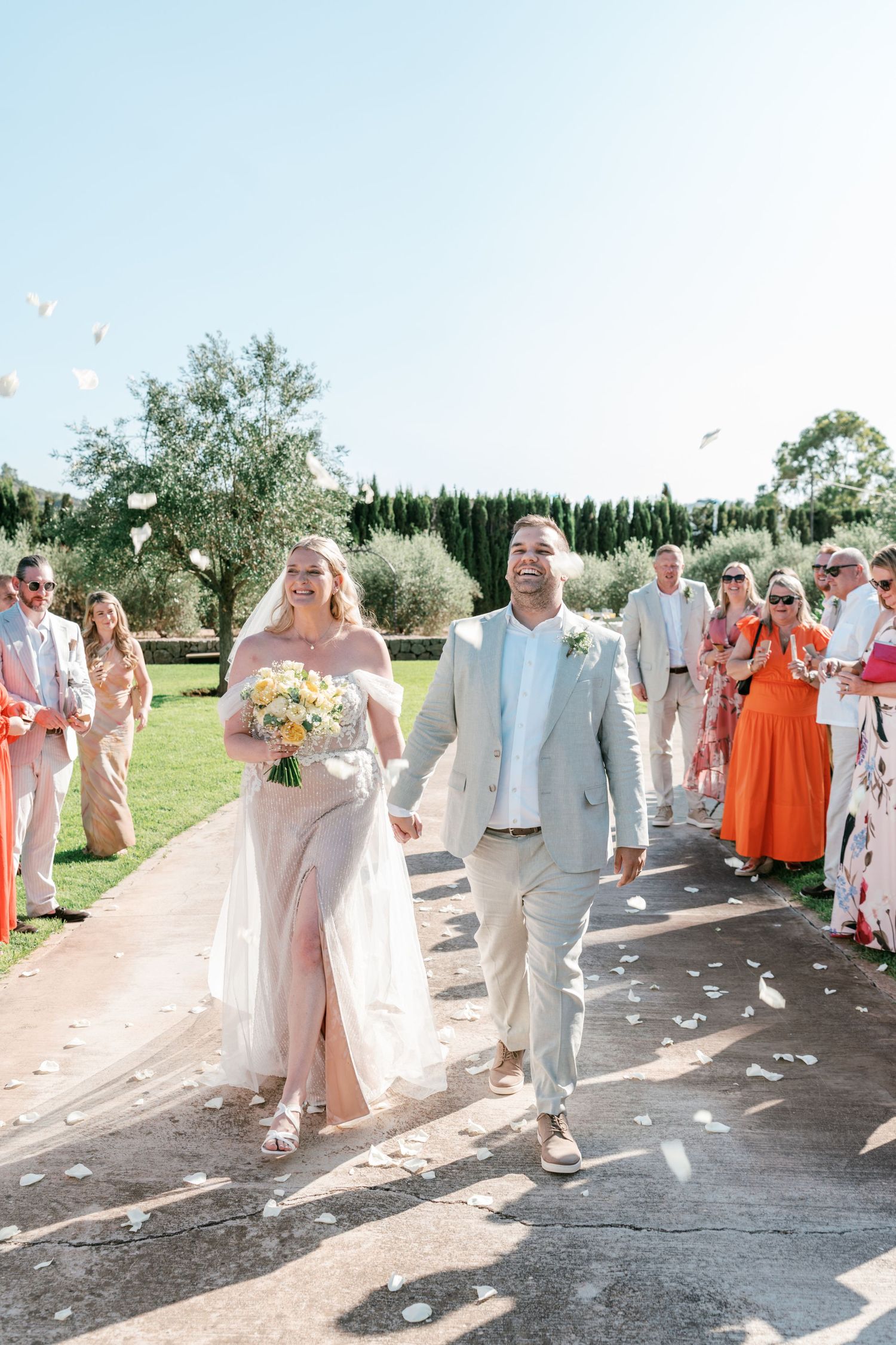 Newlyweds walk down the aisle as guests toss white petals at an outdoor Mediterranean wedding. Mallorca wedding photographer, filmmaker
