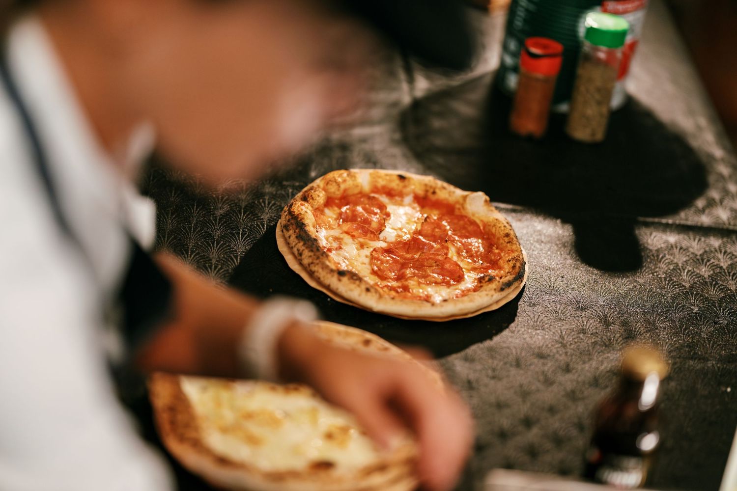 A person serves rustic Neapolitan-style pizzas with tomato sauce and melted cheese on a dark table at a wedding celebration.