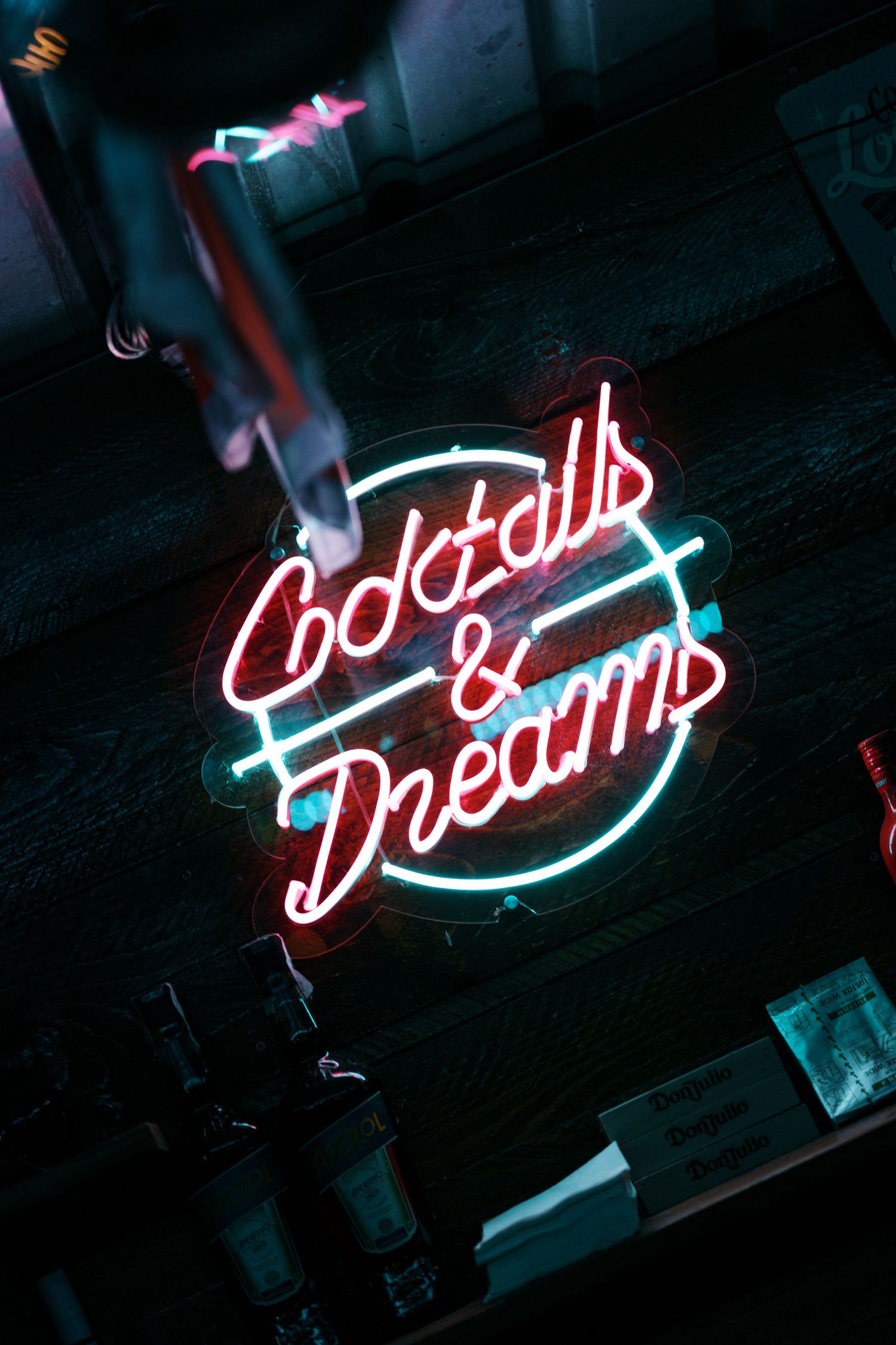 Neon sign reading Cocktails and Dreams glowing in red and blue at a dark bar.