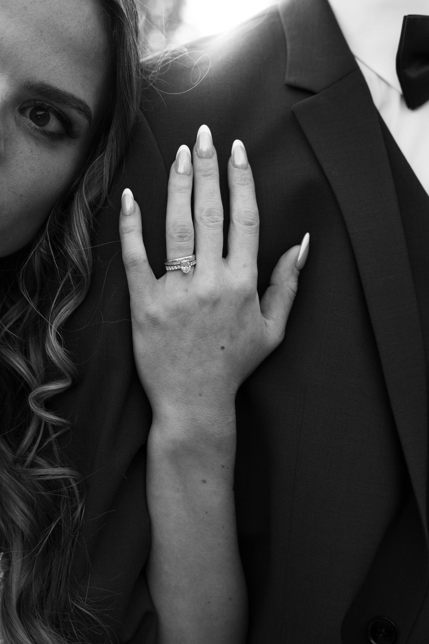 Black and white close-up of bride showing wedding ring while leaning against grooms dark suit. Mallorca wedding photographer and filmmaker.