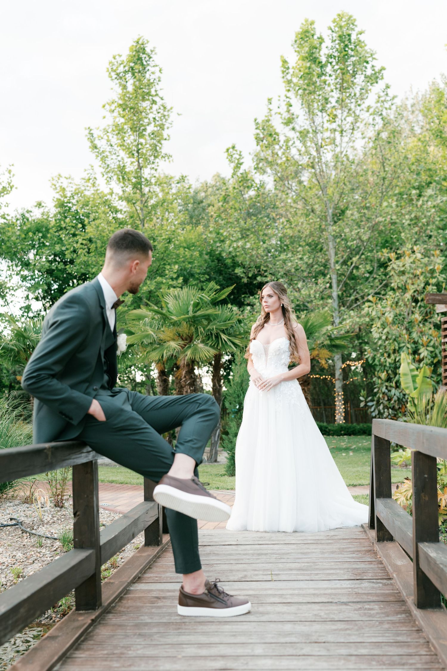 Bride and groom posing on wooden bridge surrounded by greenery at outdoor wedding venue. Mallorca wedding photographer and filmmaker.