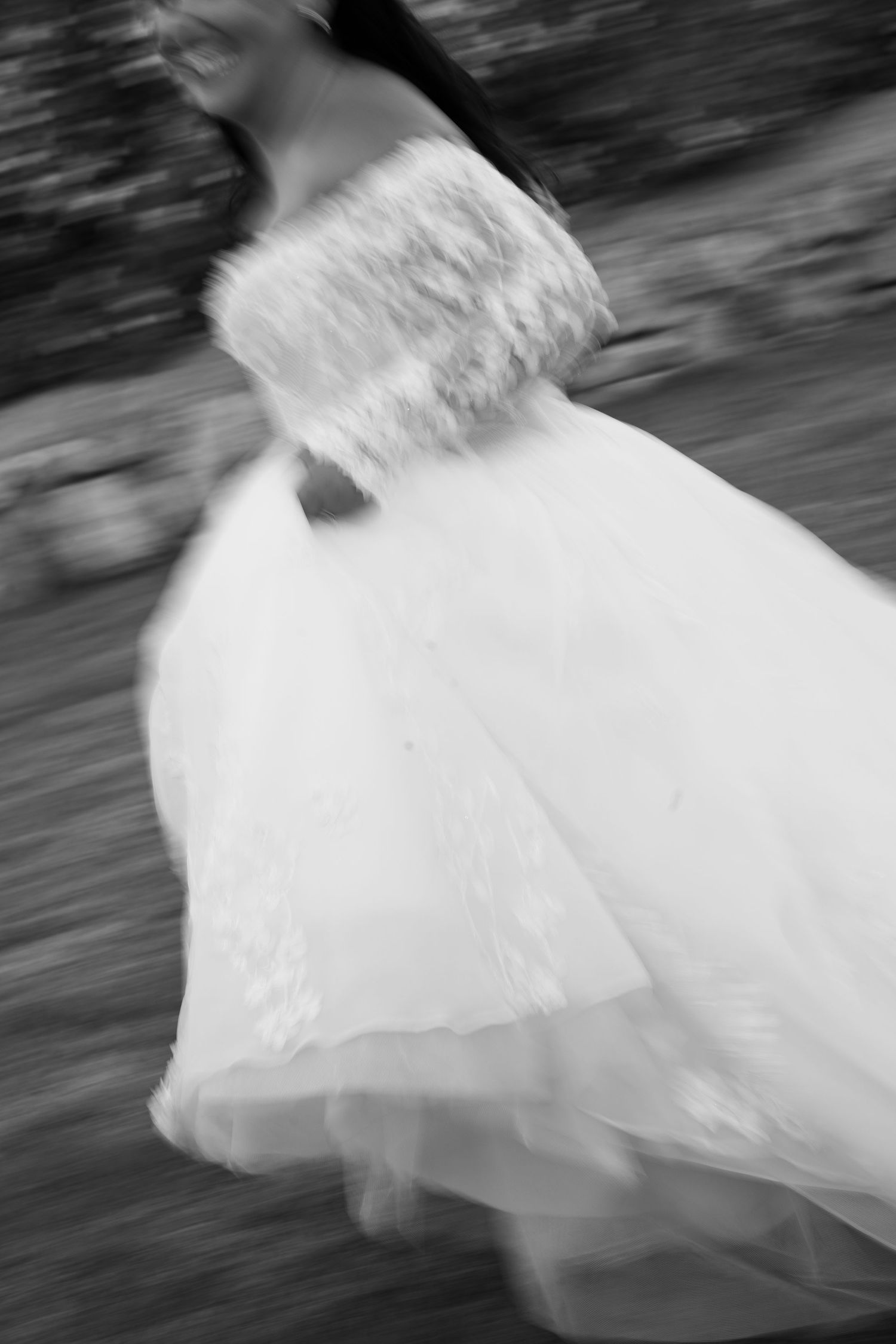 Black and white motion-blurred photo of a bride in a flowing tulle and lace off-shoulder wedding gown twirling outdoors.