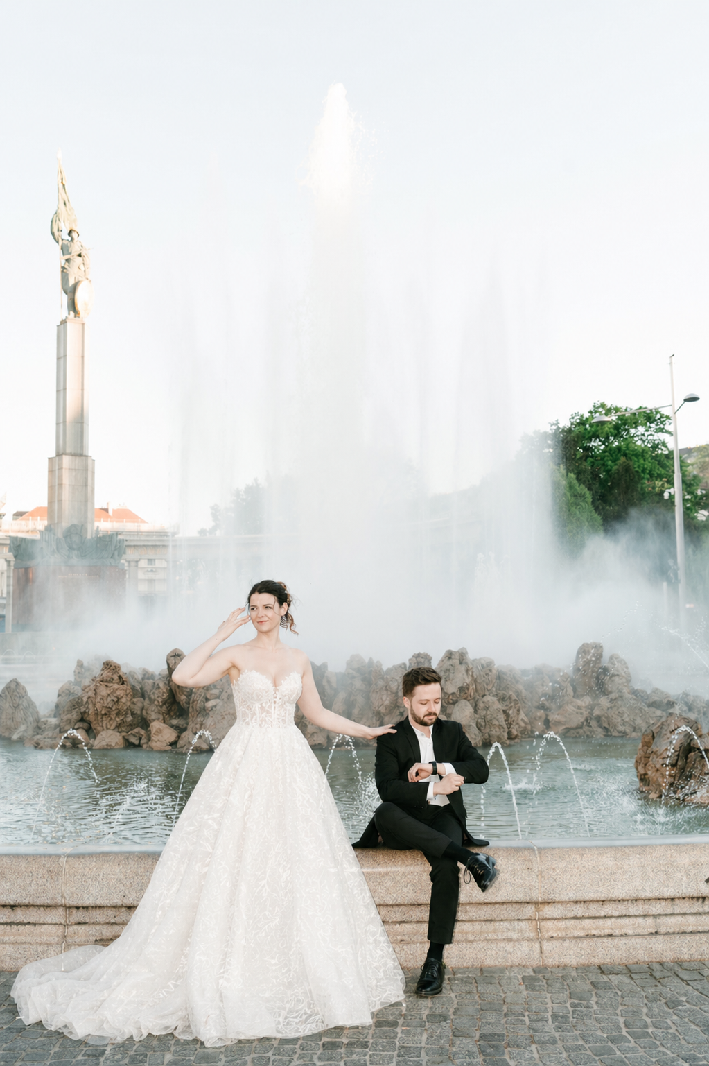 Bride and groom posing in front of grand fountain at dusk in elegant wedding attire. Mallorca wedding photographer, filmmaker