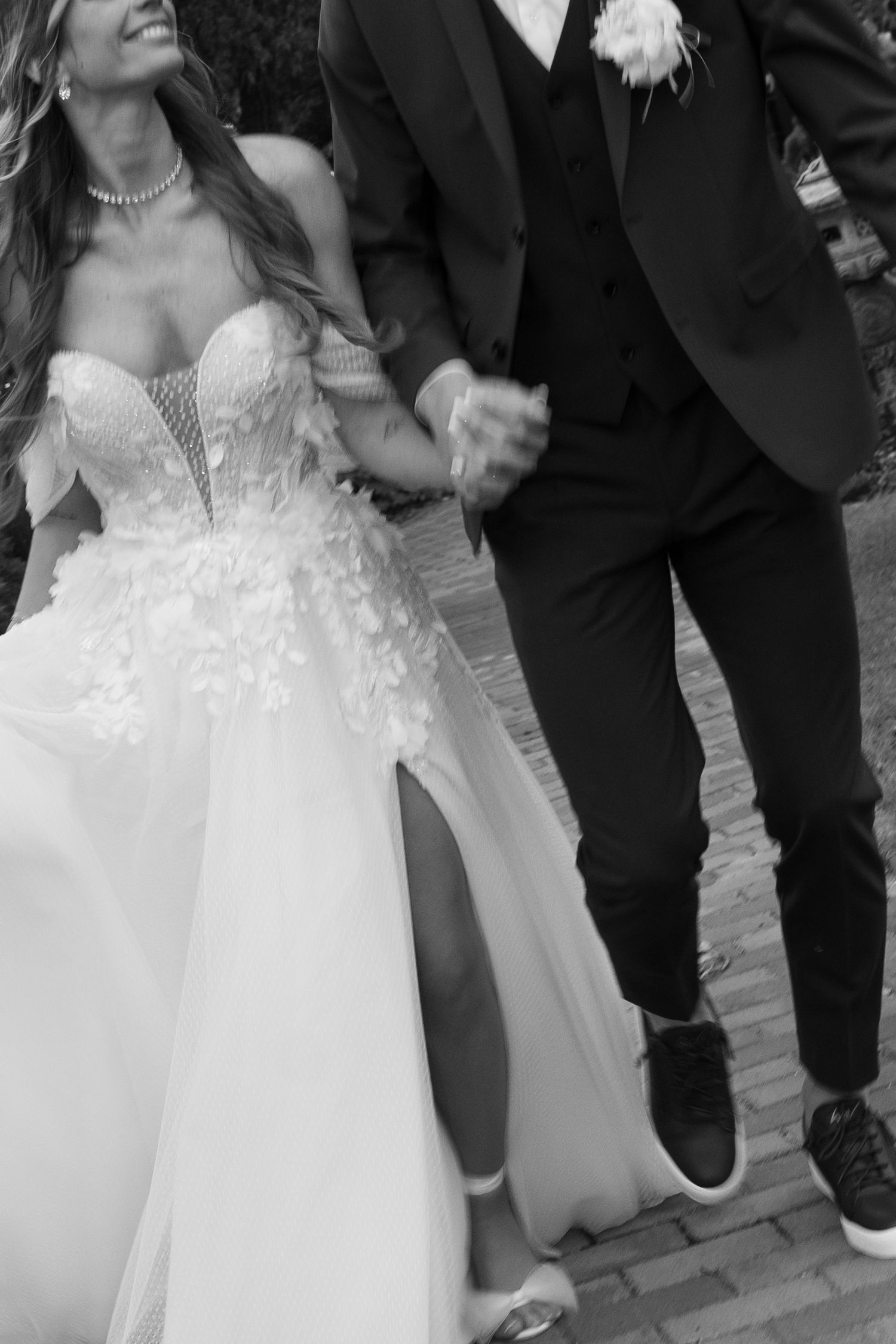 Black and white photo of smiling bride in floral wedding gown holding grooms hand while walking. Mallorca wedding photographer and filmmaker