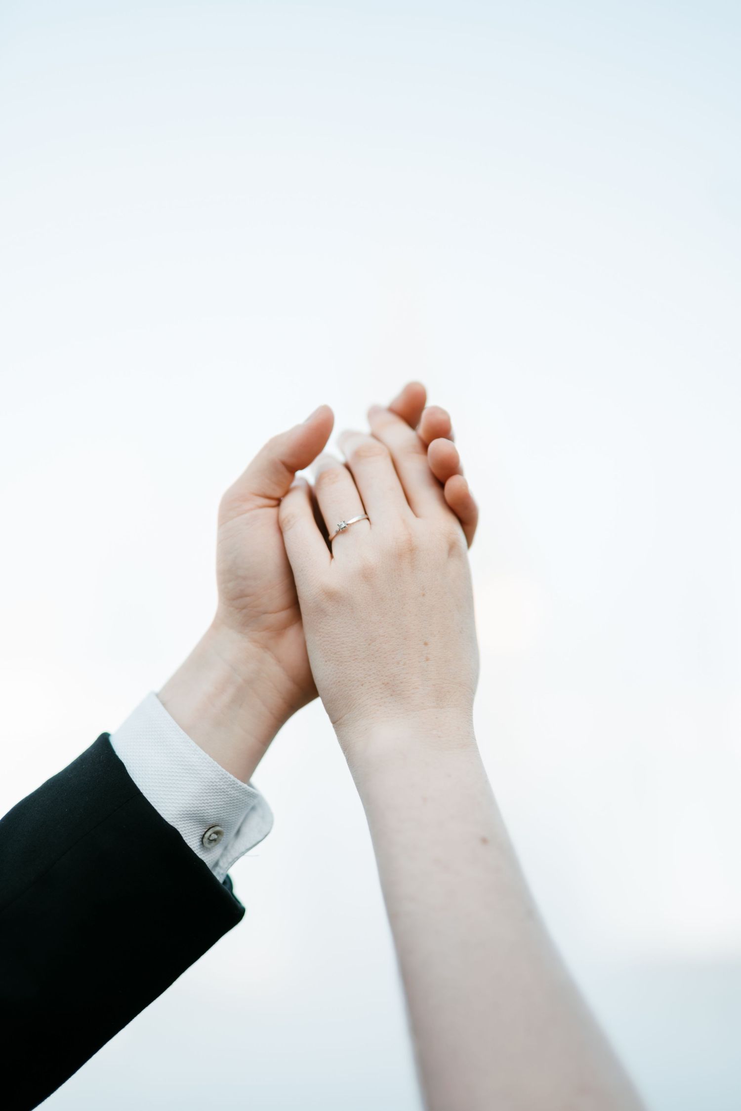 Close-up of bride and groom holding hands raised against a pale sky, wedding ring visible. Mallorca wedding photographer, filmmaker