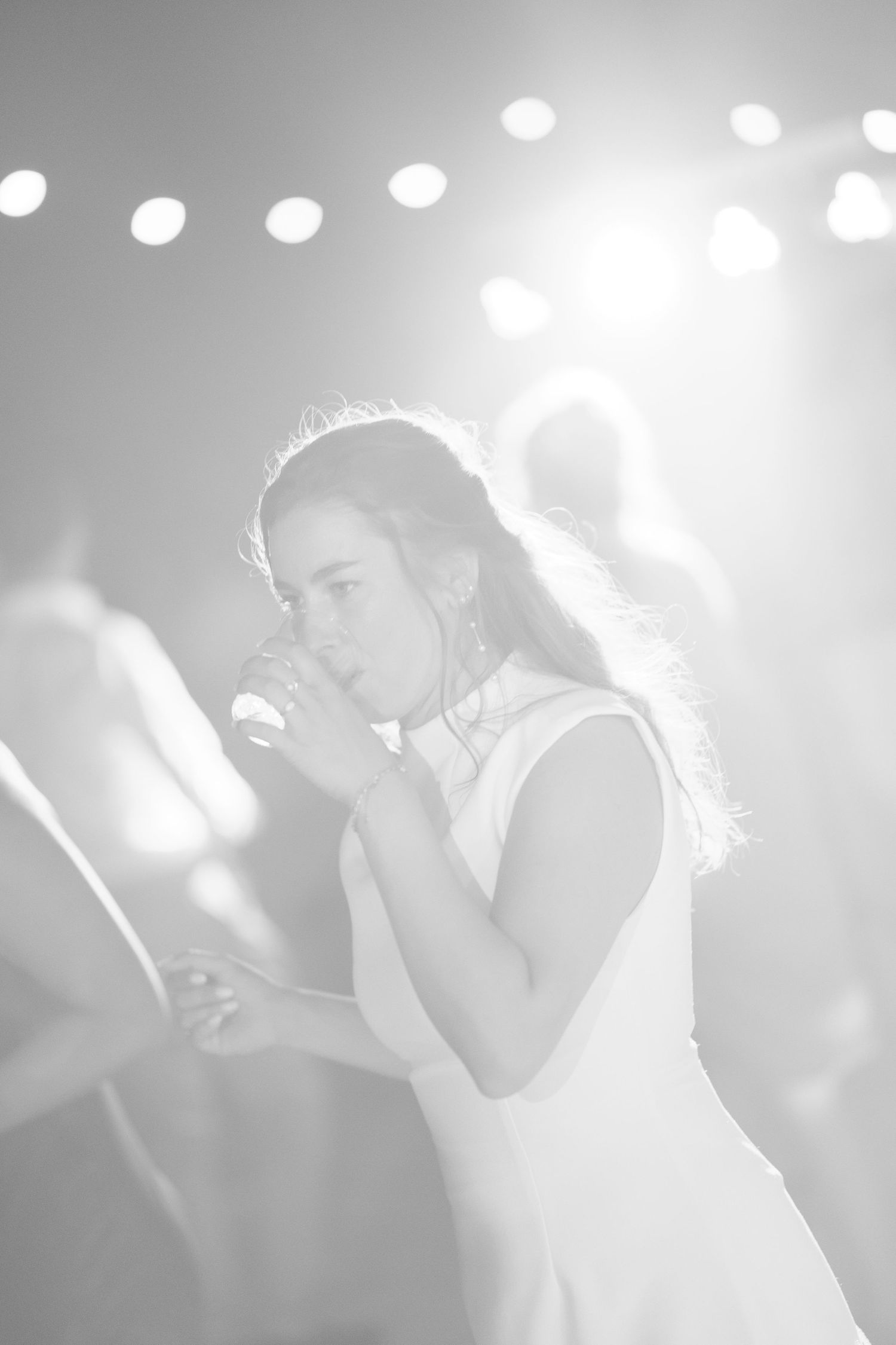 Black and white photo of a young girl singing into a microphone on stage under bright spotlights.