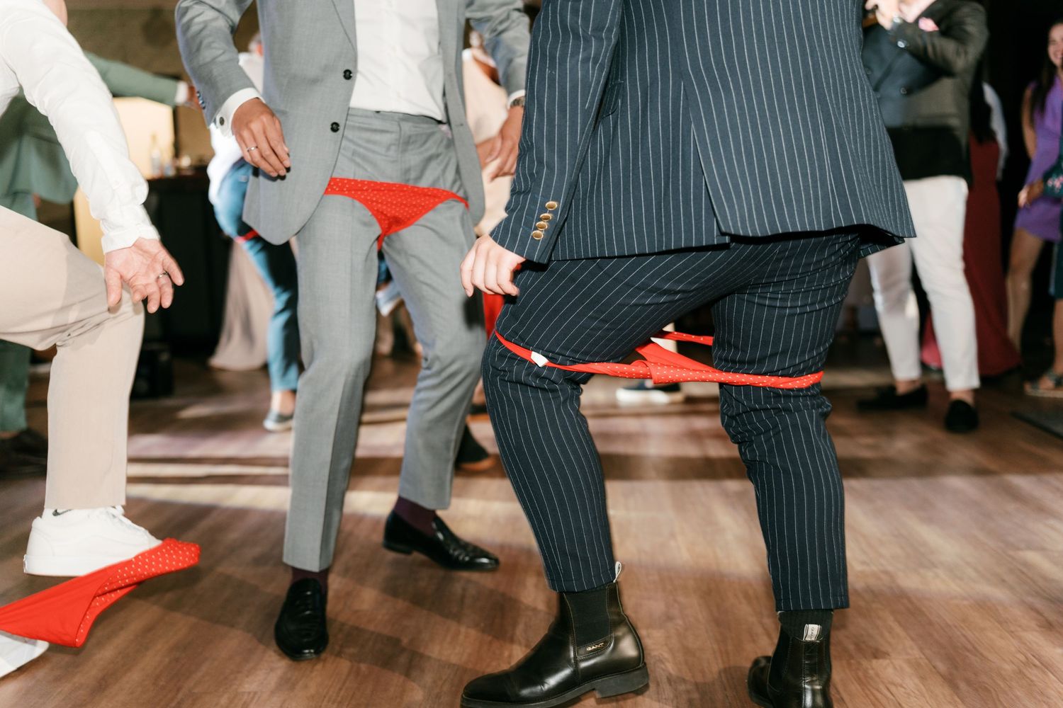 Men in suits dancing at a wedding reception with red accessories visible. Italy wedding photographer and filmmaker