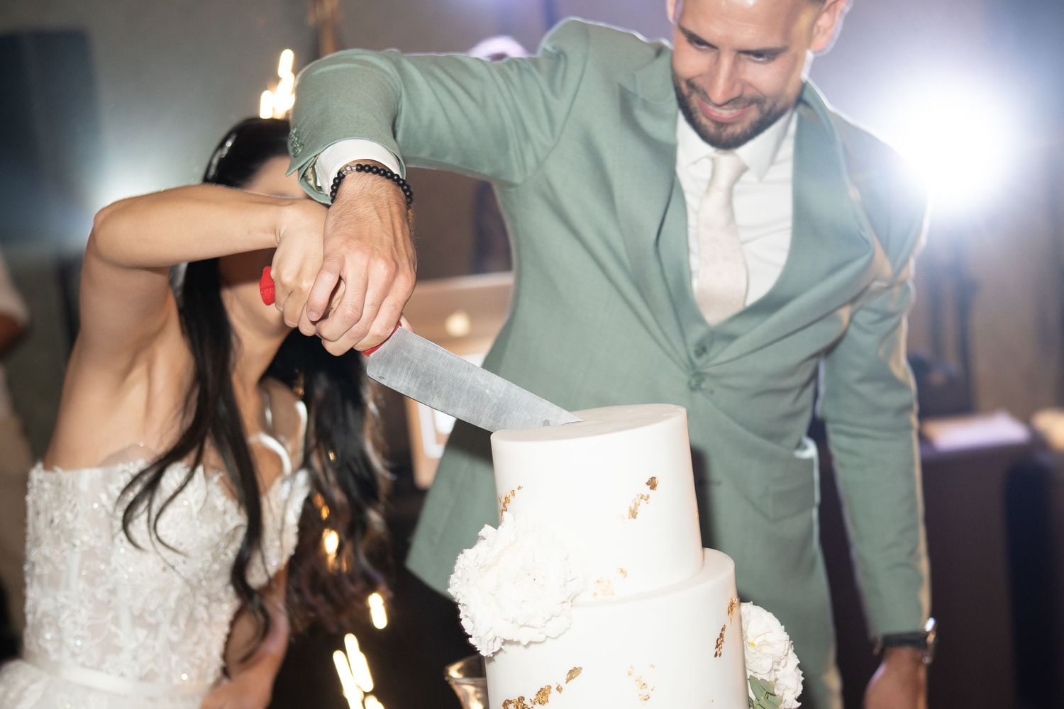 Bride and groom cutting elegant white tiered wedding cake together at reception celebration. Italy wedding photographer and filmmaker