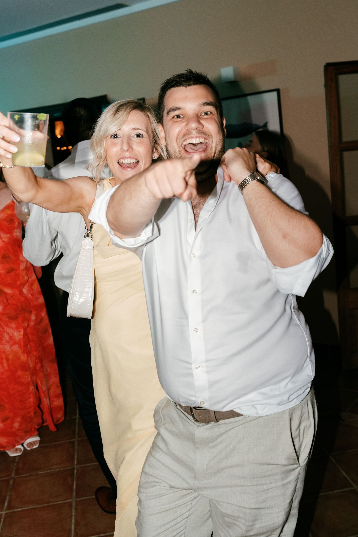 Joyful wedding guests smiling and pointing at camera while celebrating at evening reception party. Tuscany wedding photographer, filmmaker