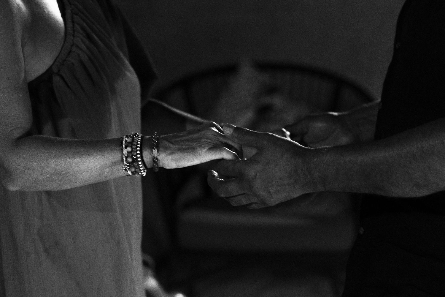 Close-up black and white photo of two people holding hands with bracelets visible.