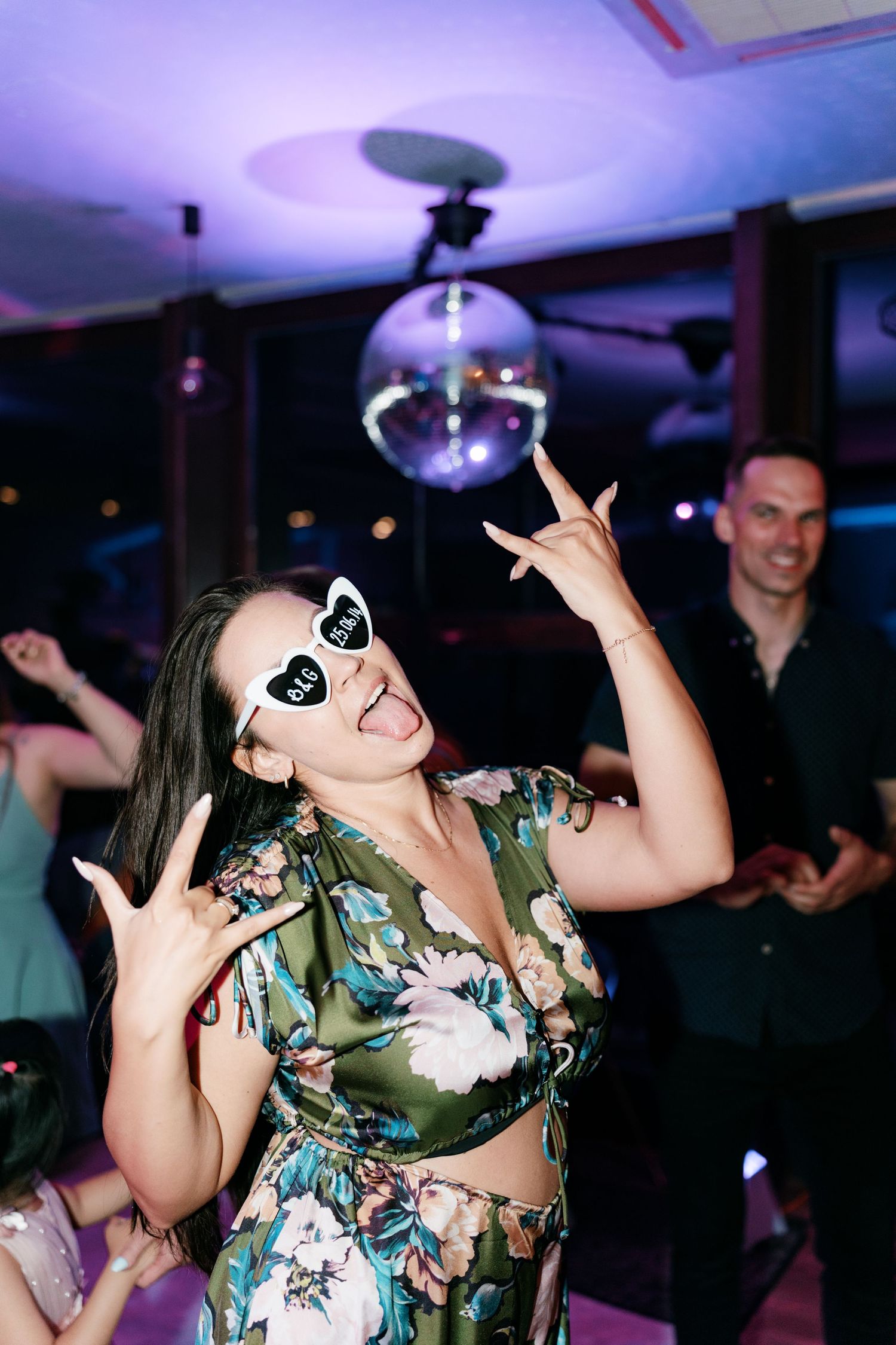 Woman in floral dress with heart sunglasses dancing under disco ball at party. Italy wedding photographer