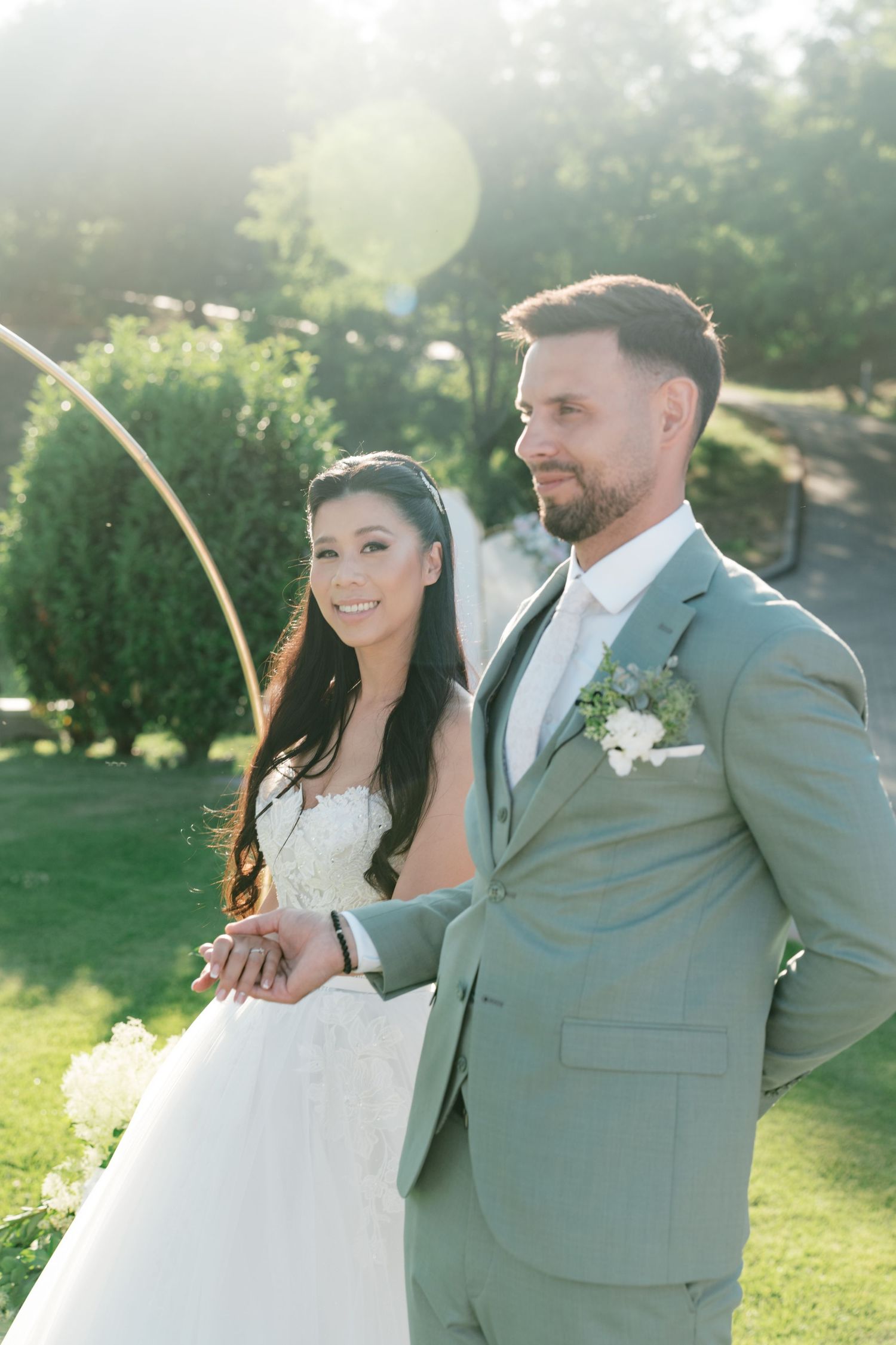 Smiling bride and groom standing together at a circular arch in golden sunlight outdoors. Italy wedding photographer and filmmaker