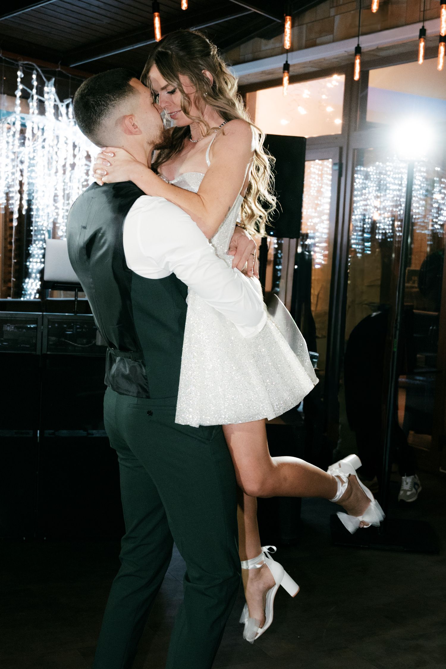 Groom lifts smiling bride in short sparkly white dress during joyful first dance at wedding reception. Mallorca wedding photographer