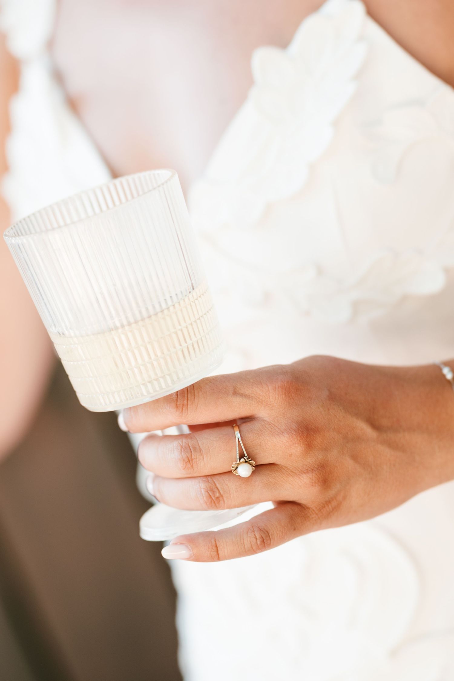 Bride in white dress holding ribbed candle holder, wearing delicate gold engagement ring with small diamond.