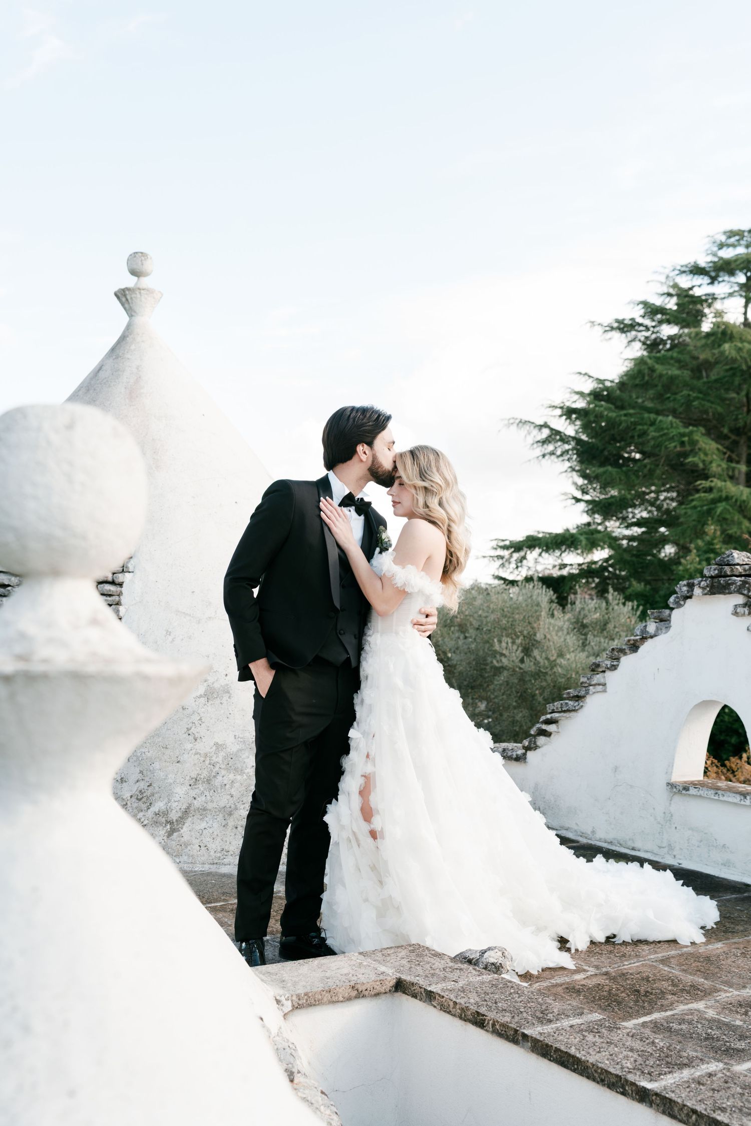Romantic wedding couple kissing on a rooftop terrace with white trulli domes and cypress trees. Mallorca wedding photographer, filmmaker