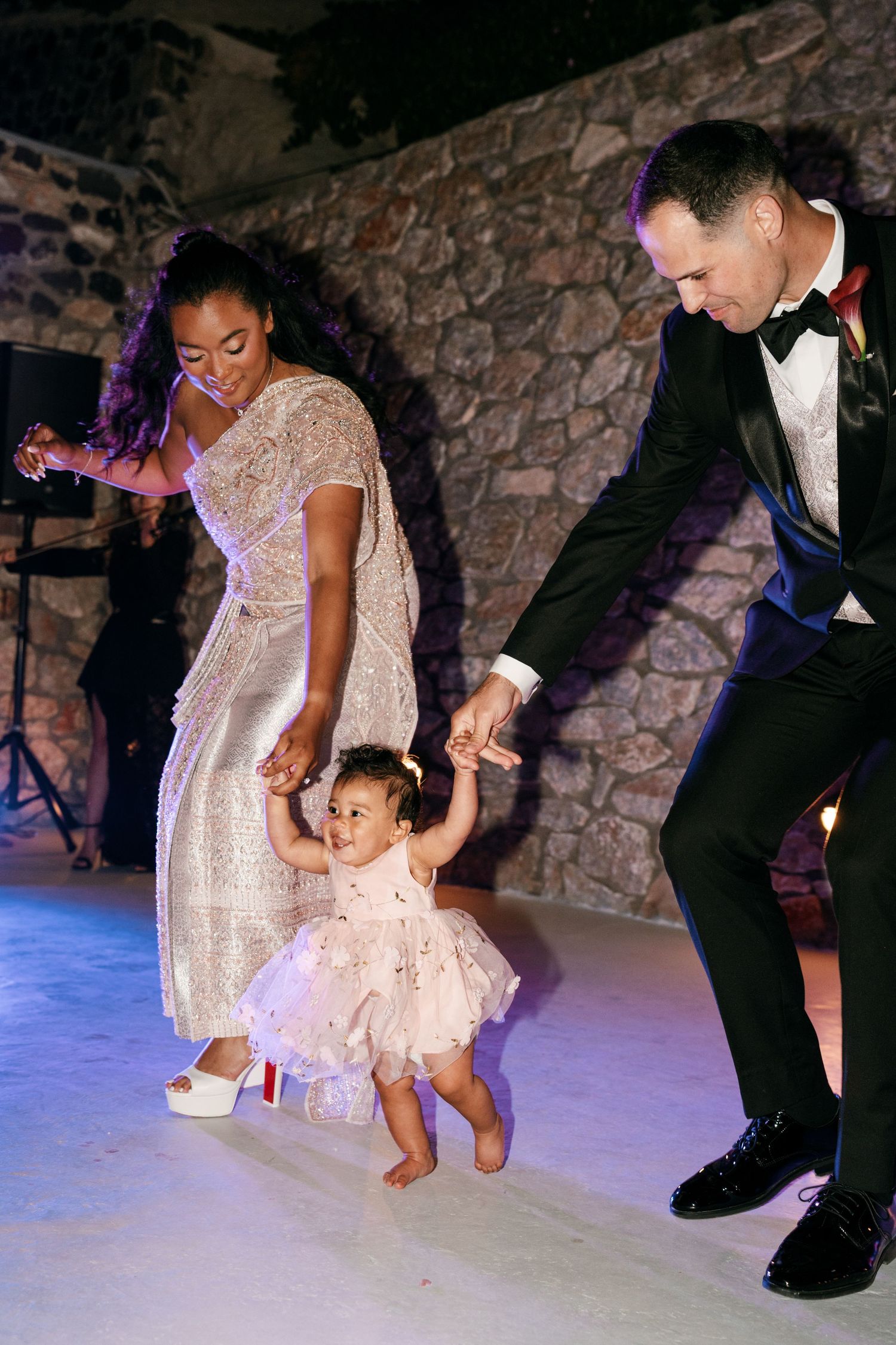 Bride and groom in formal attire dancing with their toddler daughter on a wedding reception dance floor.