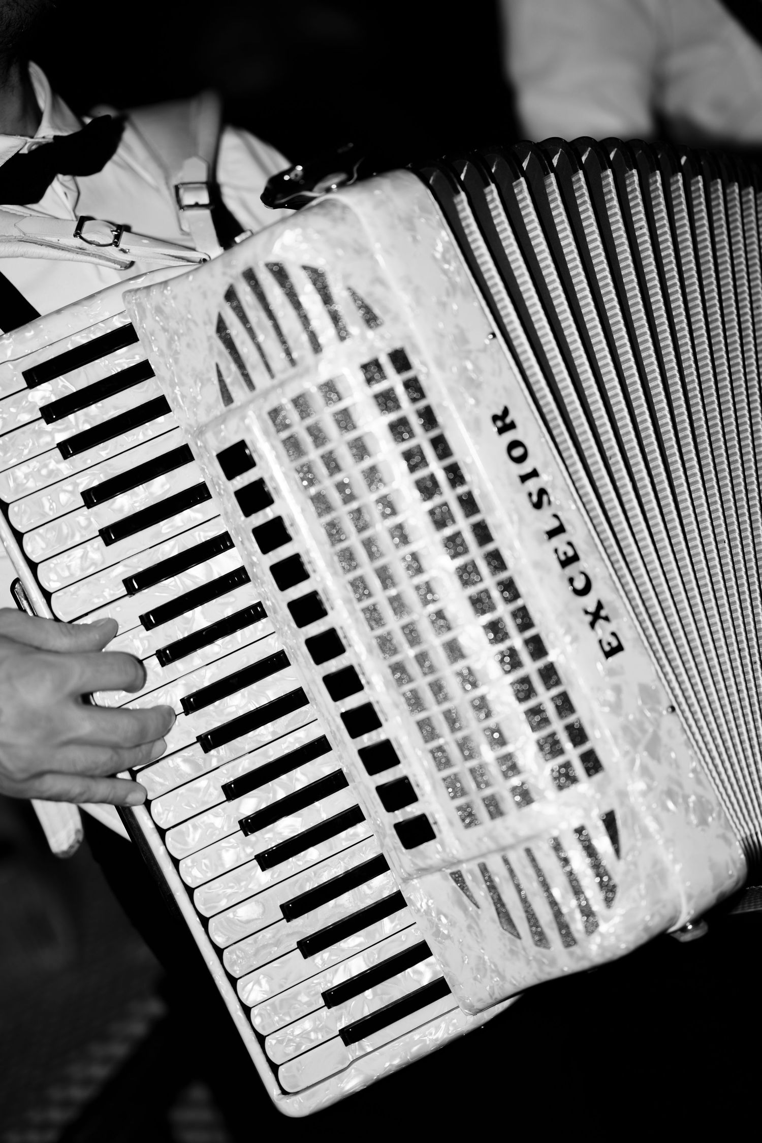 Black and white photo of hands playing a vintage Excelsior piano accordion, showcasing the keys and bellows.