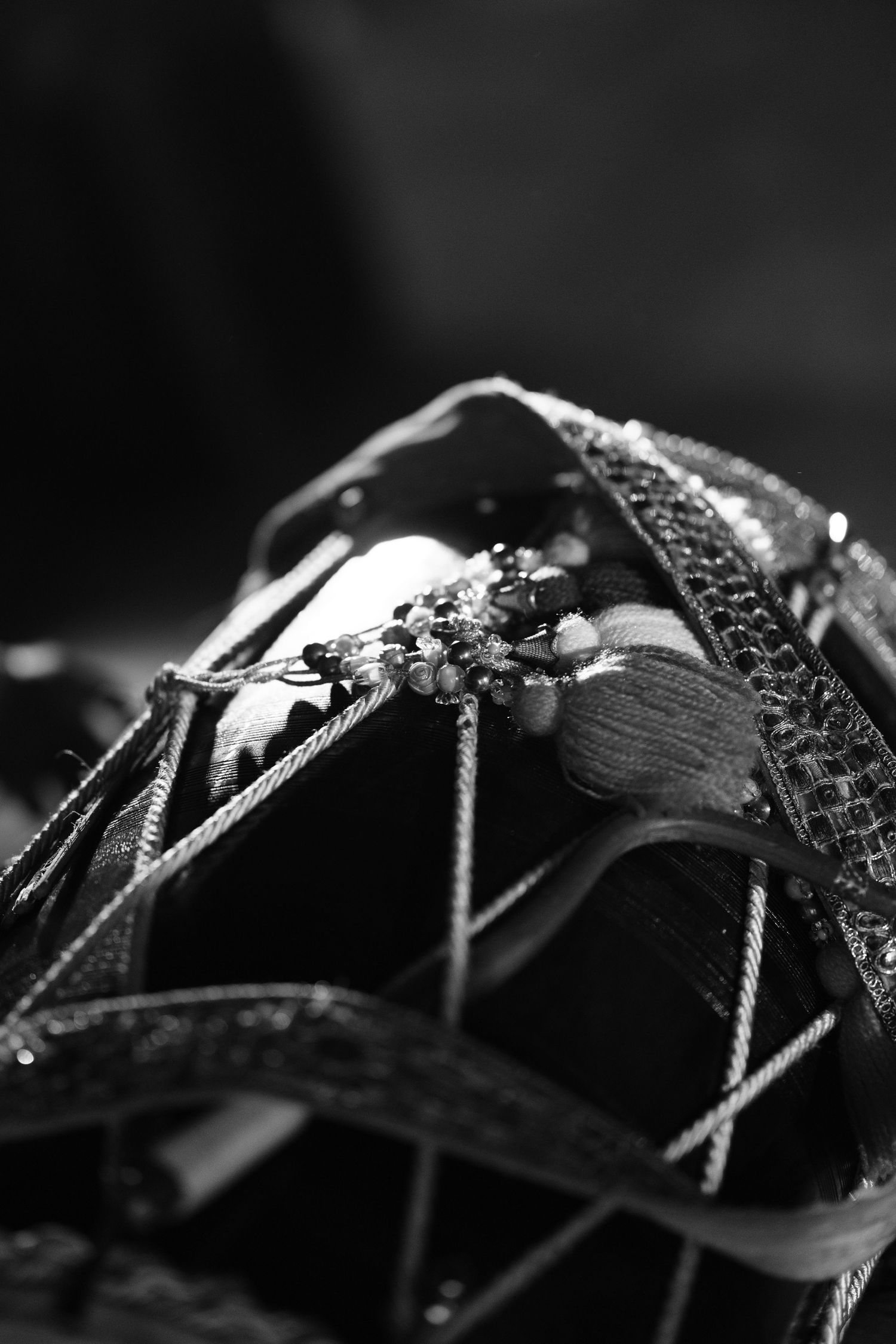 Black and white close-up of ornate beaded and embroidered wedding accessories with delicate cords and decorative trim.