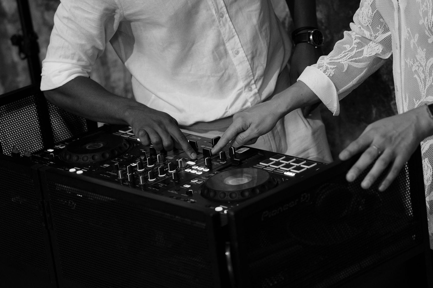 Black and white photo of a DJ in a white shirt mixing music on a professional controller with turntable jog wheels and knobs.