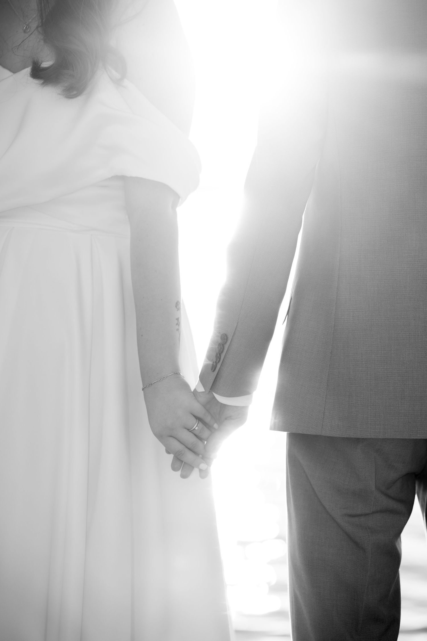 Black and white close-up of bride and groom holding hands in bright sunlight. Mallorca wedding photographer, filmmaker
