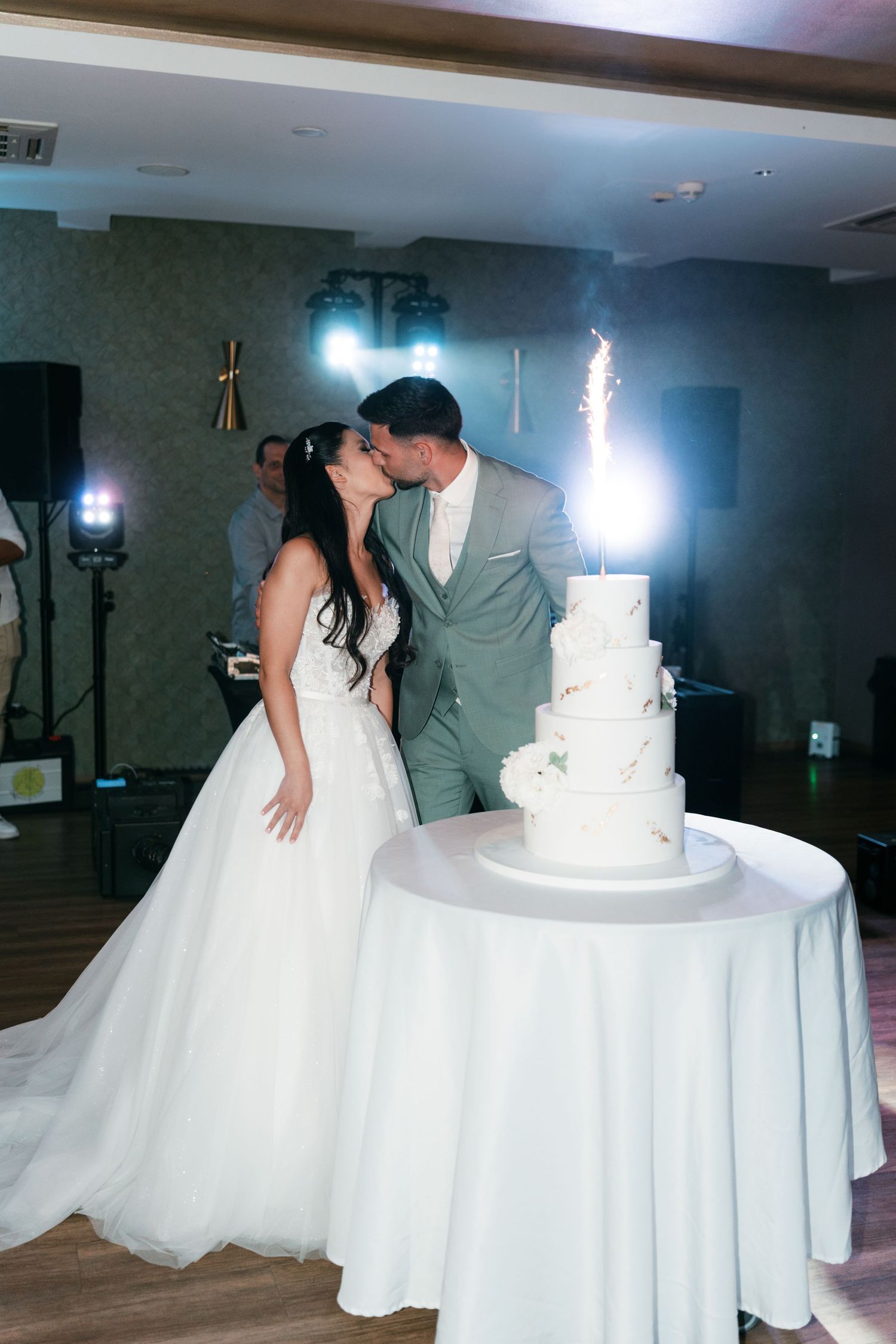 Bride and groom share a kiss beside their four-tier white wedding cake with sparklers. Italy wedding photographer and filmmaker