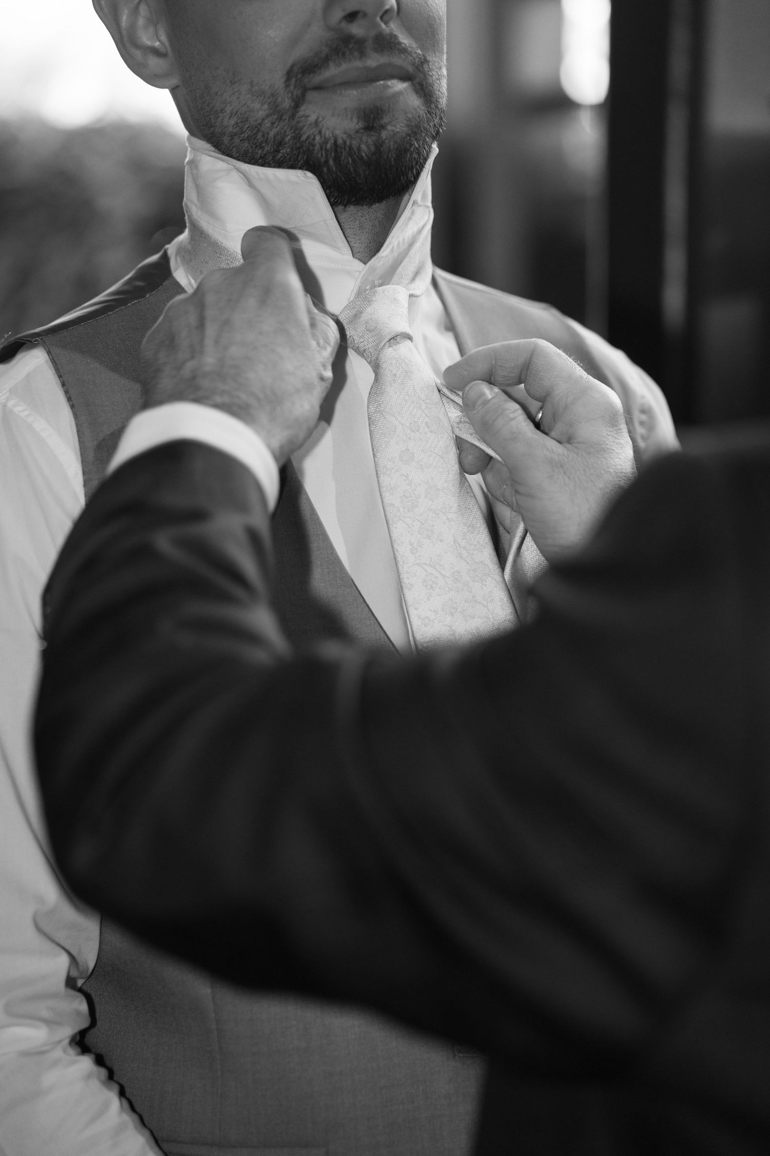 Black and white close-up of a man adjusting a grooms floral tie before the wedding. Italy wedding photographer and filmmaker