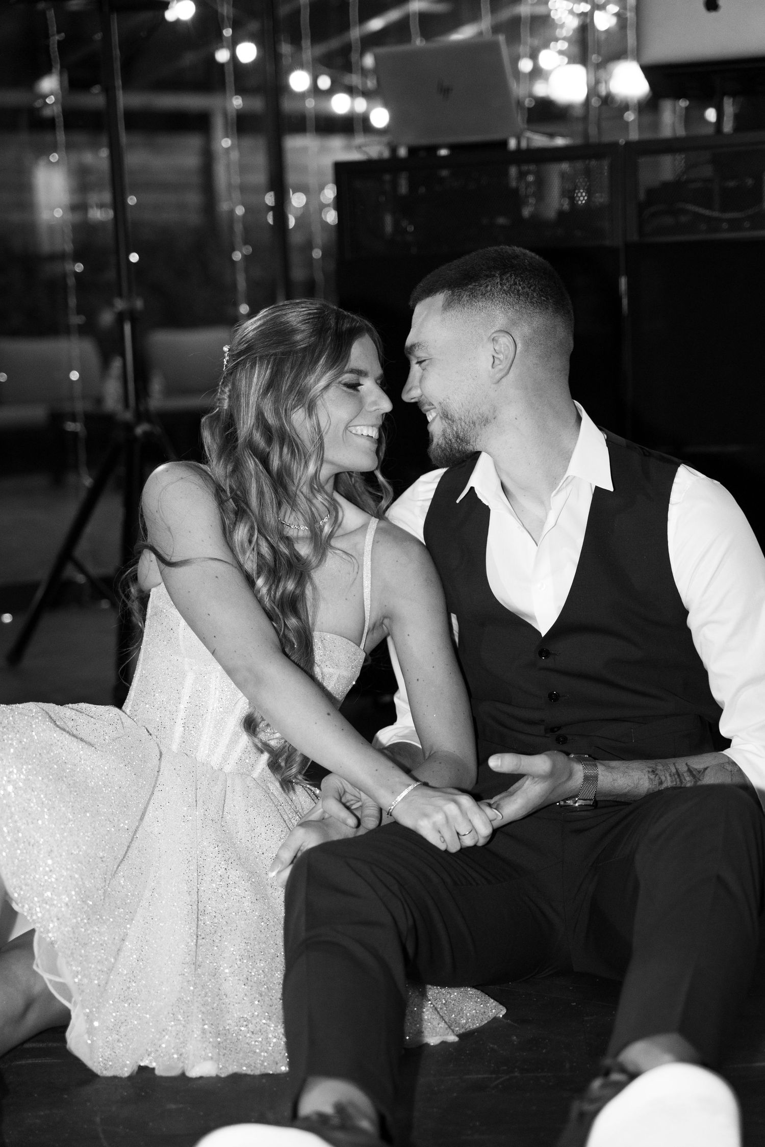 Black and white photo of smiling bride and groom sitting together holding hands at wedding reception. Mallorca wedding photographer and film