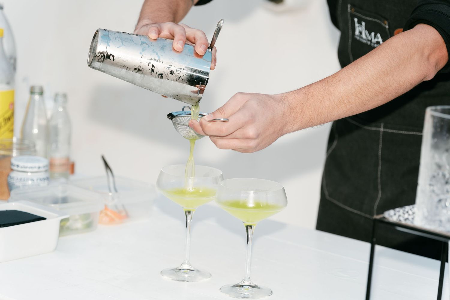 Bartender pouring green cocktails from a shaker into coupe glasses at a wedding reception bar. Puglia wedding photographer, film