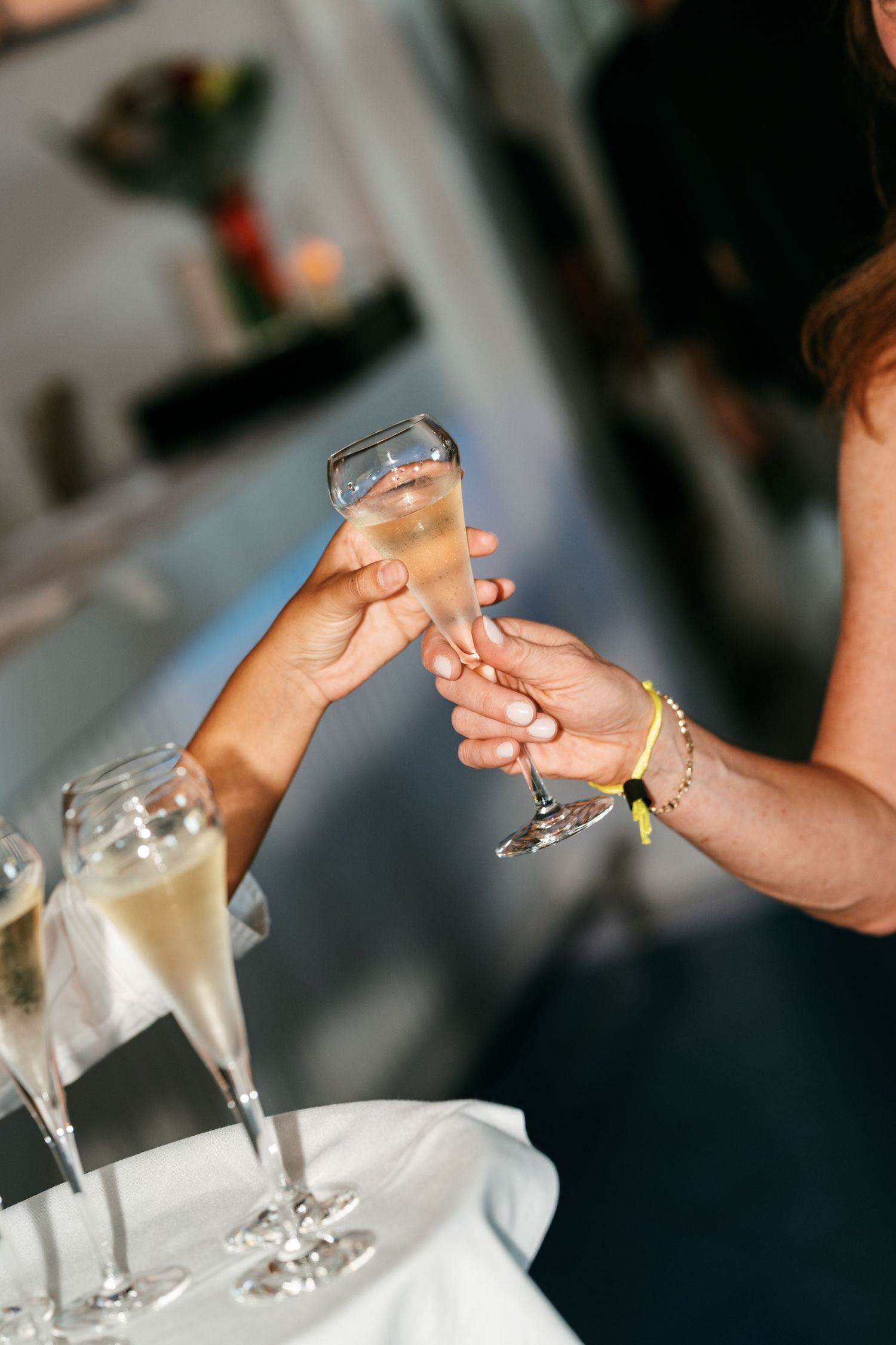 A guest hands a flute of sparkling champagne to another person, with more filled glasses resting on a white tablecloth nearby.