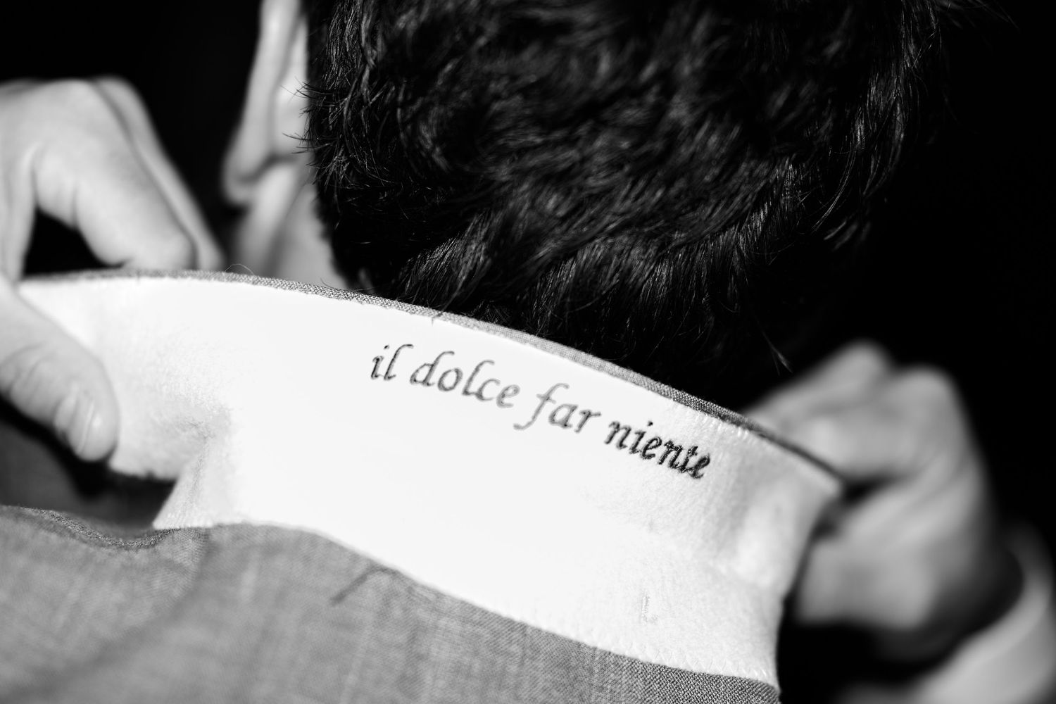 Close-up of a neck tattoo reading 'il dolce far niente' in elegant script on a man in a suit.