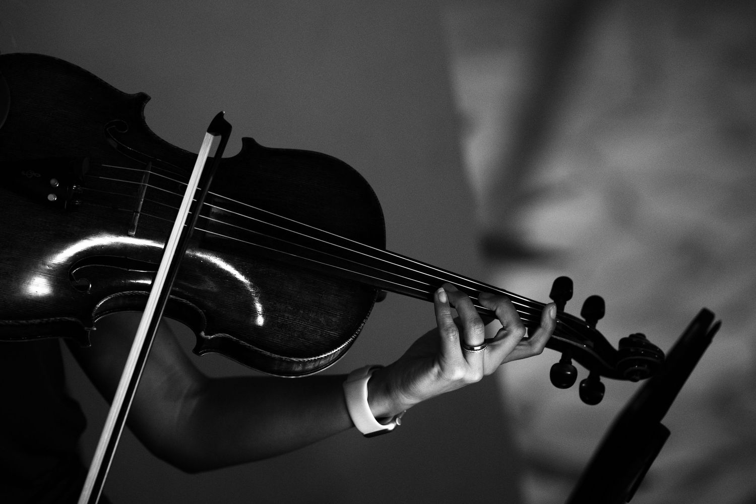 Black and white close-up of a violinist's hand pressing the strings of a violin while the bow glides across during a live performance.