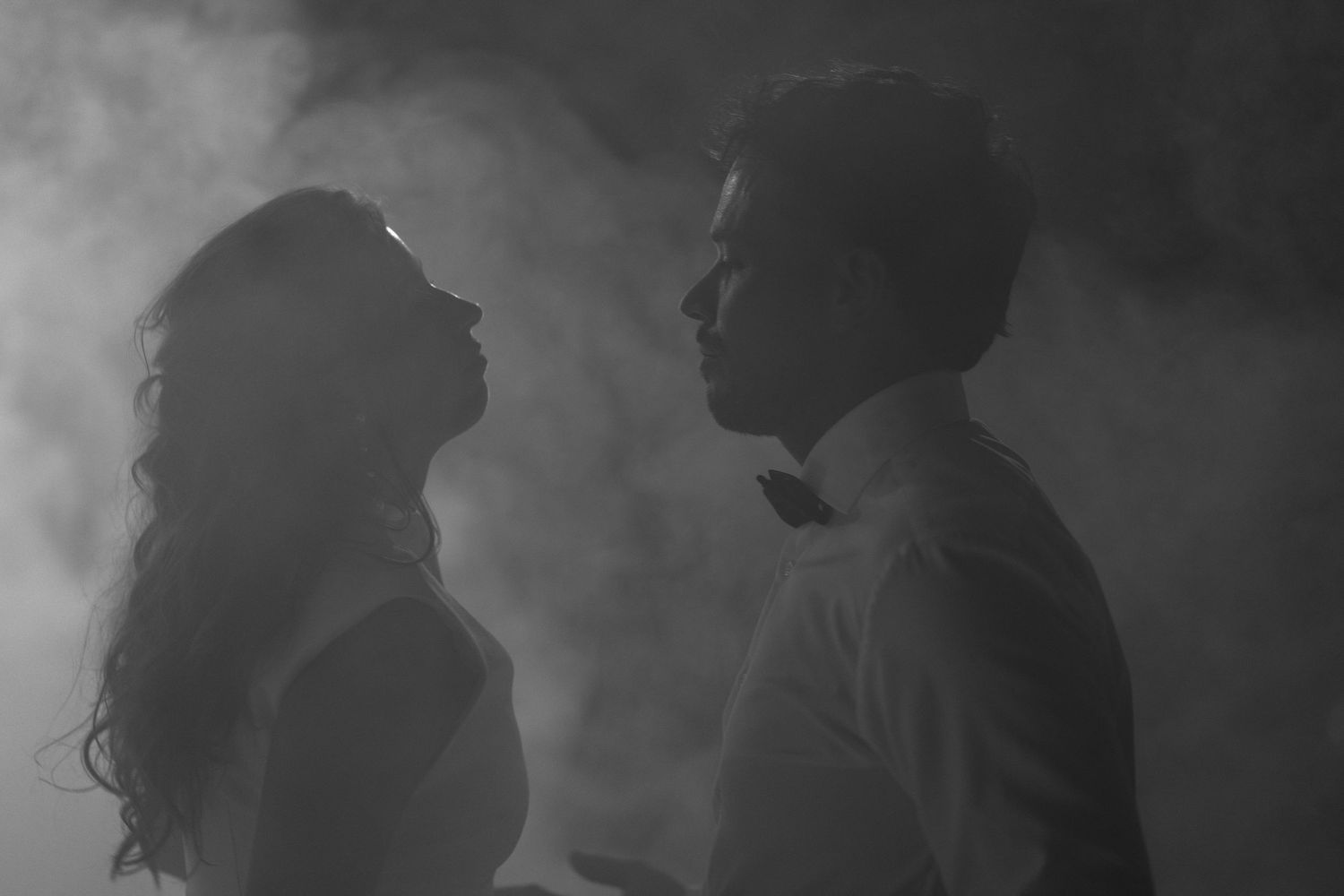 Romantic black and white silhouette of a bride and groom surrounded by misty smoke at their wedding.