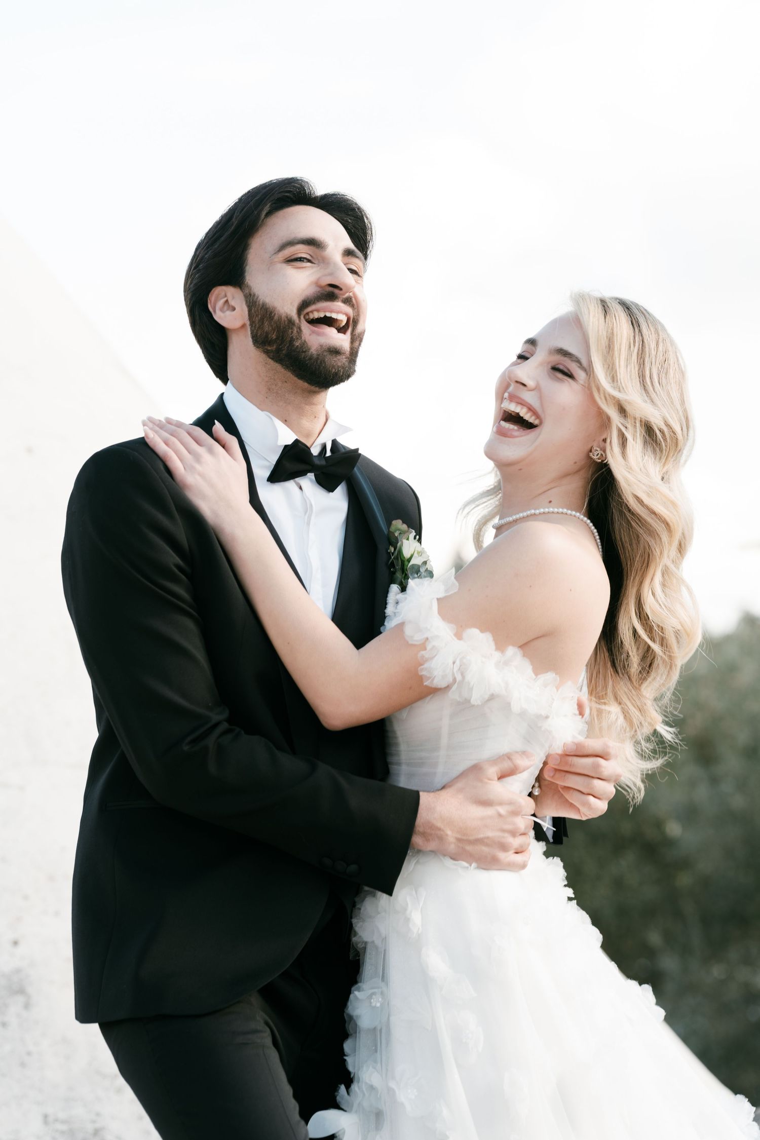Laughing bride and groom embrace joyfully outdoors on their sunny wedding day in Italy. Puglia wedding photographer, film
