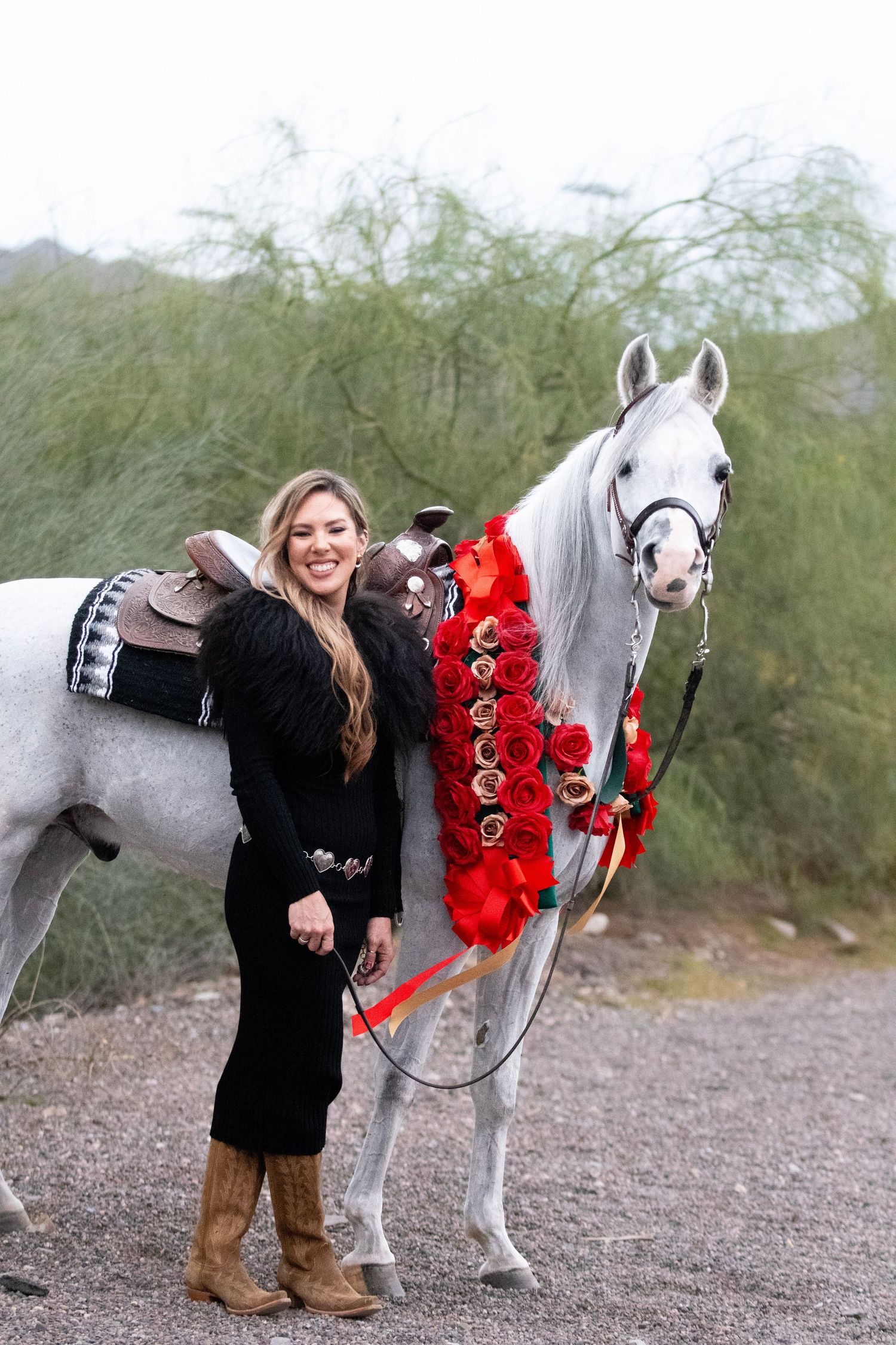 Adult woman and white horse stand next to each with garlands on.