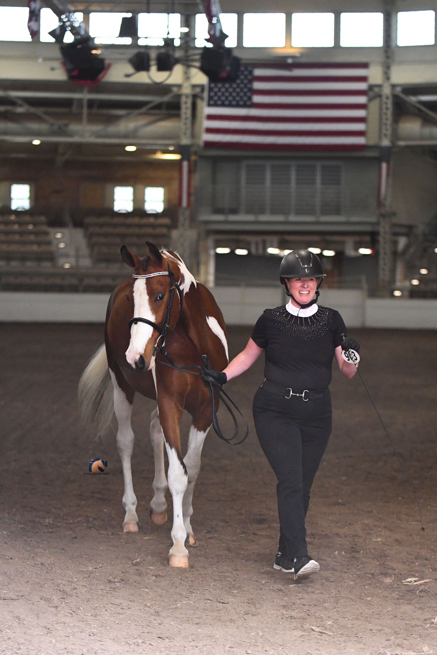 Pinto horse with adult woman walking out of arena.