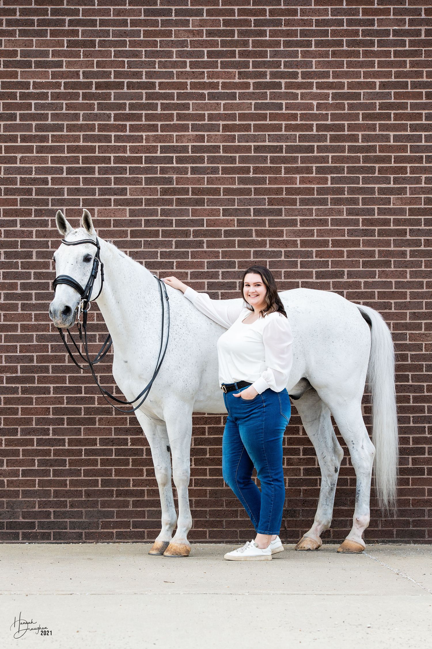 Adult woman and white horse in front of brick wall