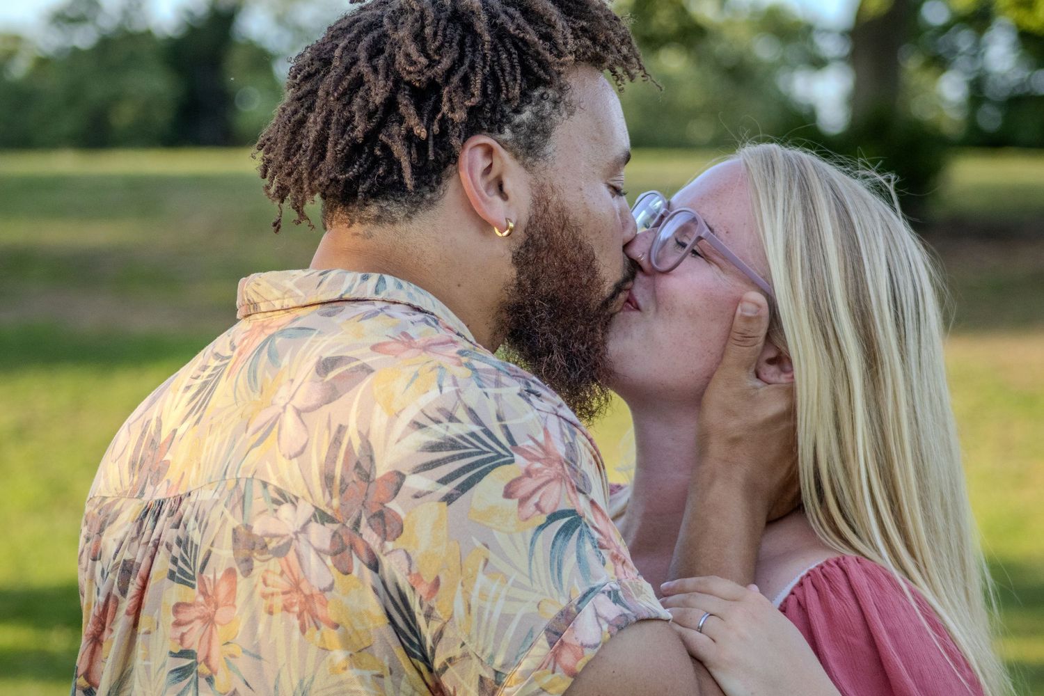 Couple shares a kiss outdoors in a sunny green park setting.