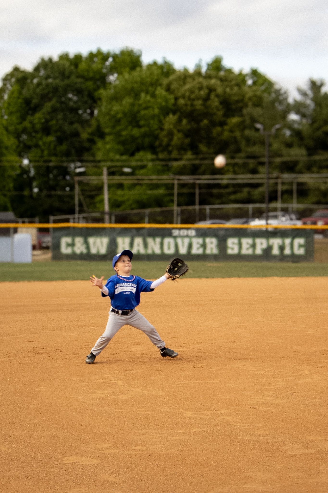 Young boy in blue baseball uniform catching a fly ball in the outfield during a game.