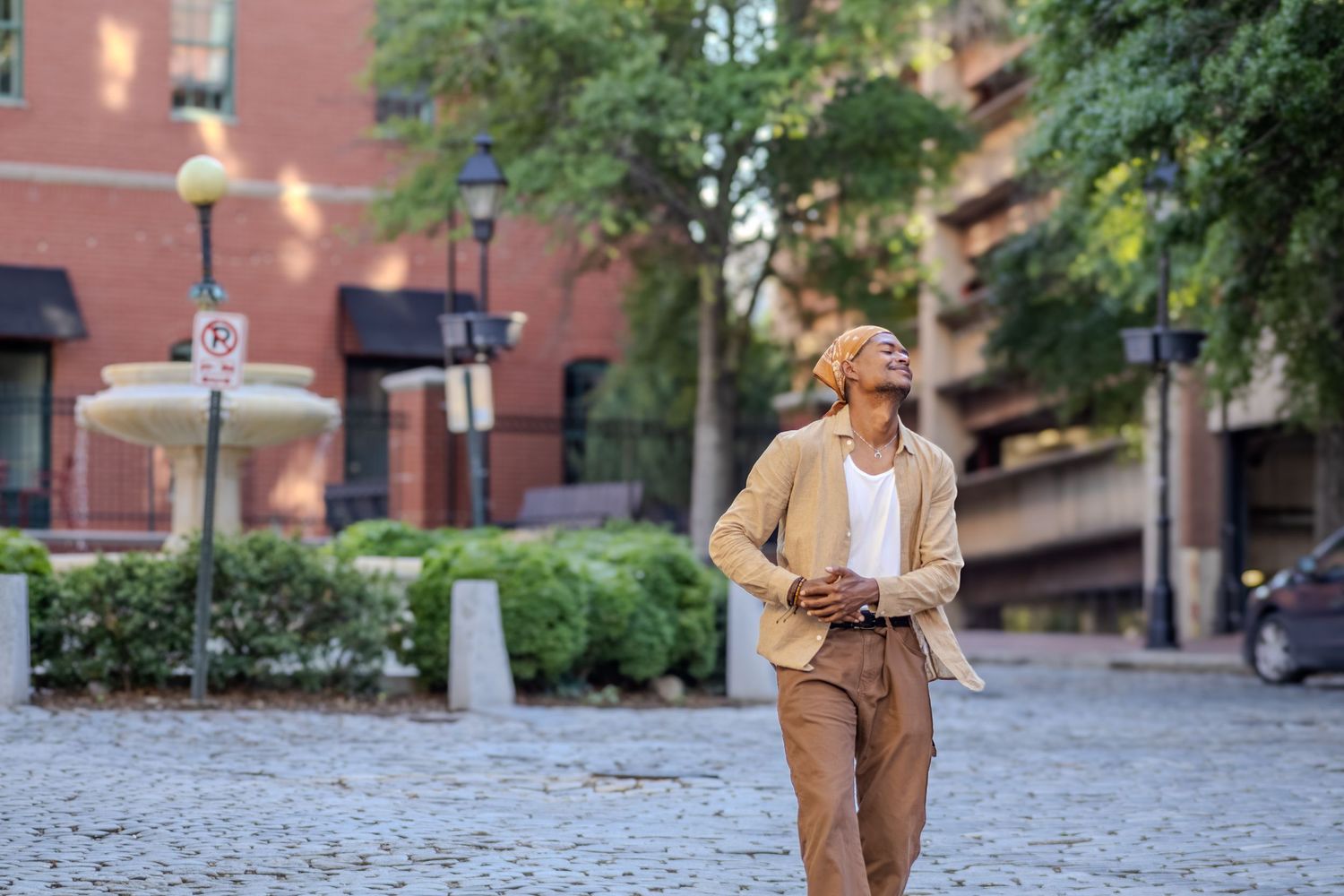 Fashionable woman in beige suit walks on cobblestone street in urban neighborhood.