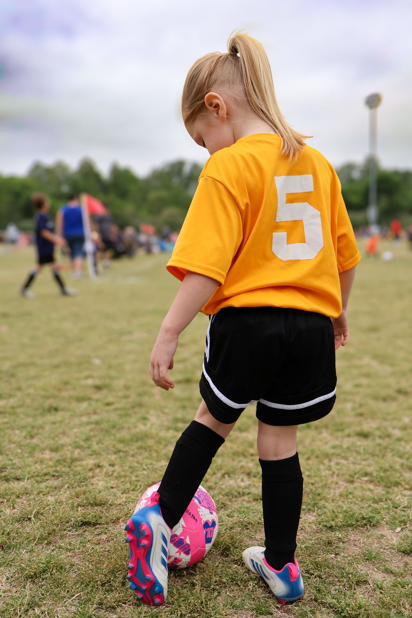 A young girl in a yellow number 5 soccer jersey dribbles a ball on a green field.