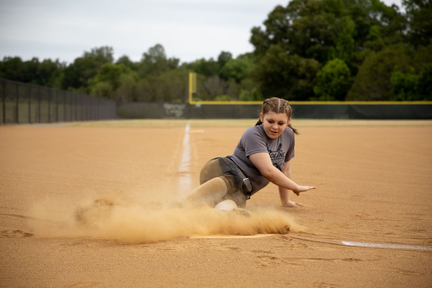 Girl on softball field with dust flying