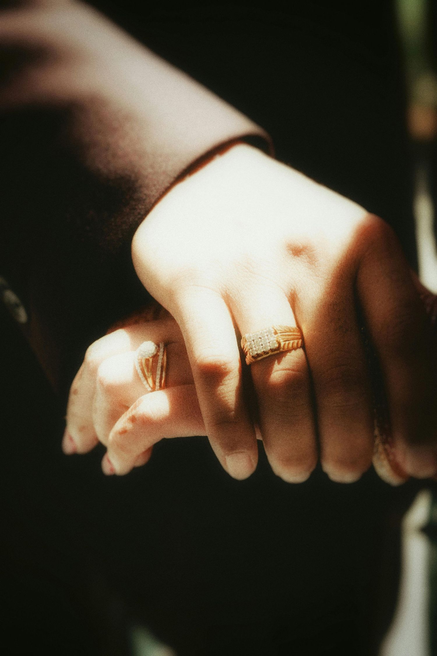 Close-up of couple holding hands wearing matching gold wedding rings in warm sunlight.